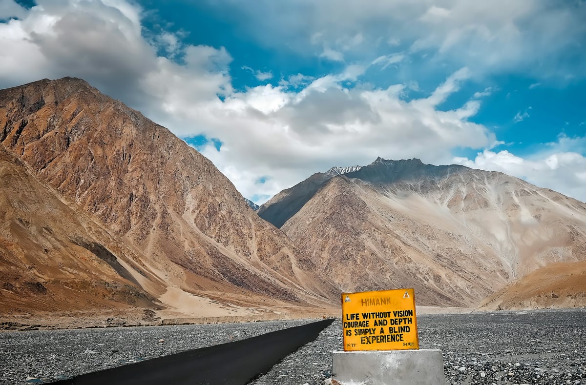 A yellow warning sign beside a gravel road in a bare high-altitude valley