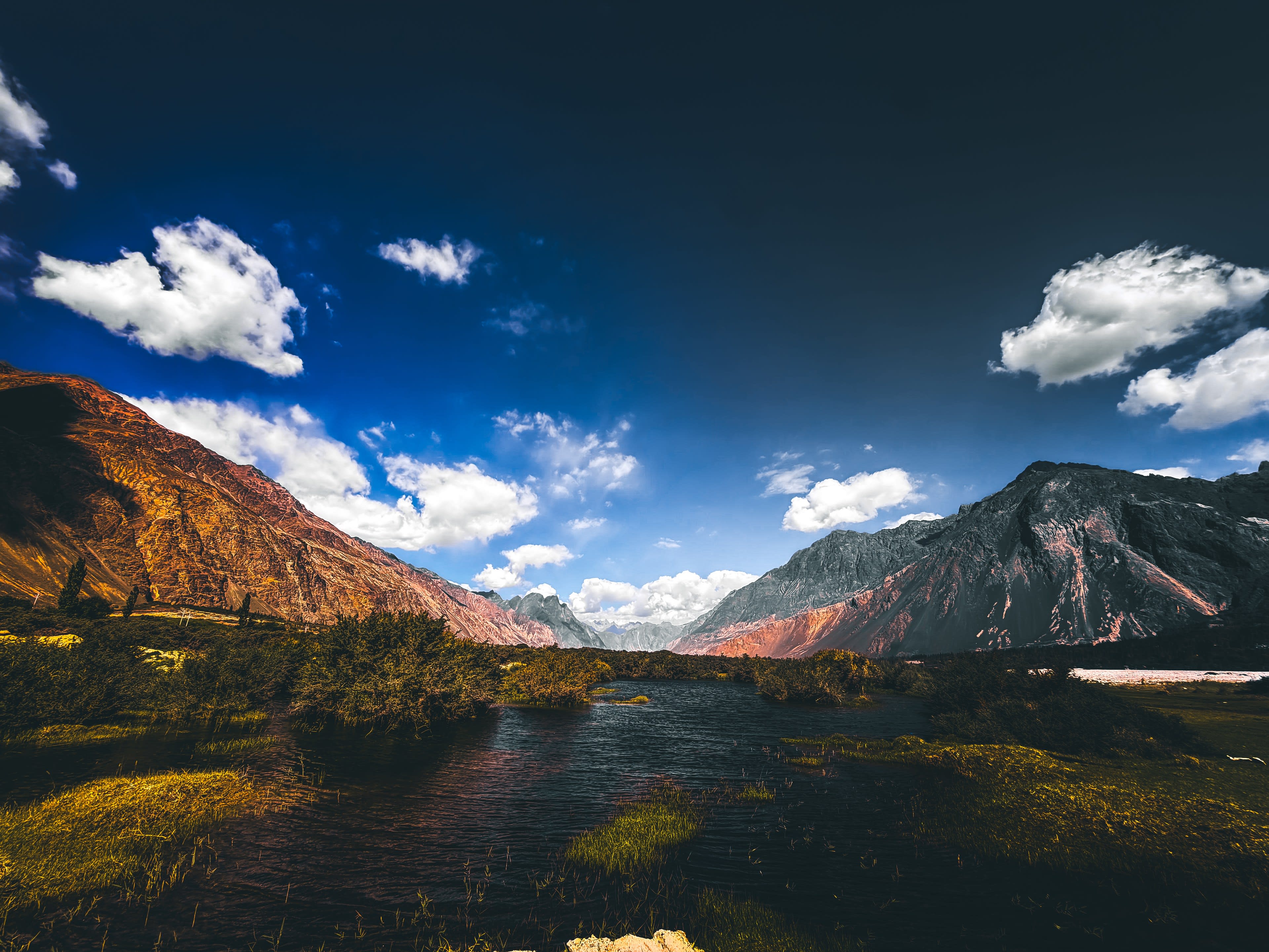A green river valley between bare mountains under a blue sky