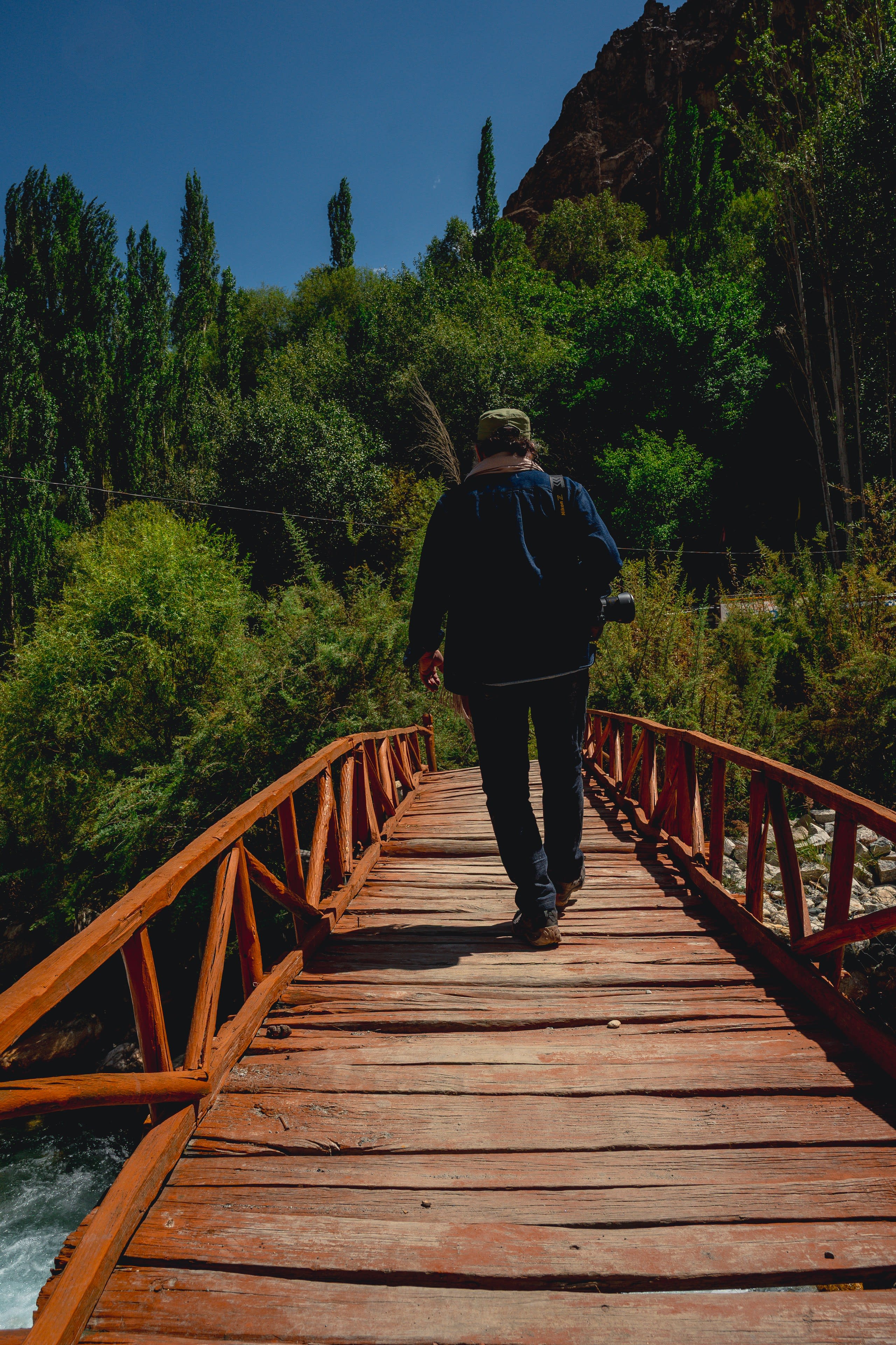 A man crossing a wooden footbridge into dense green trees