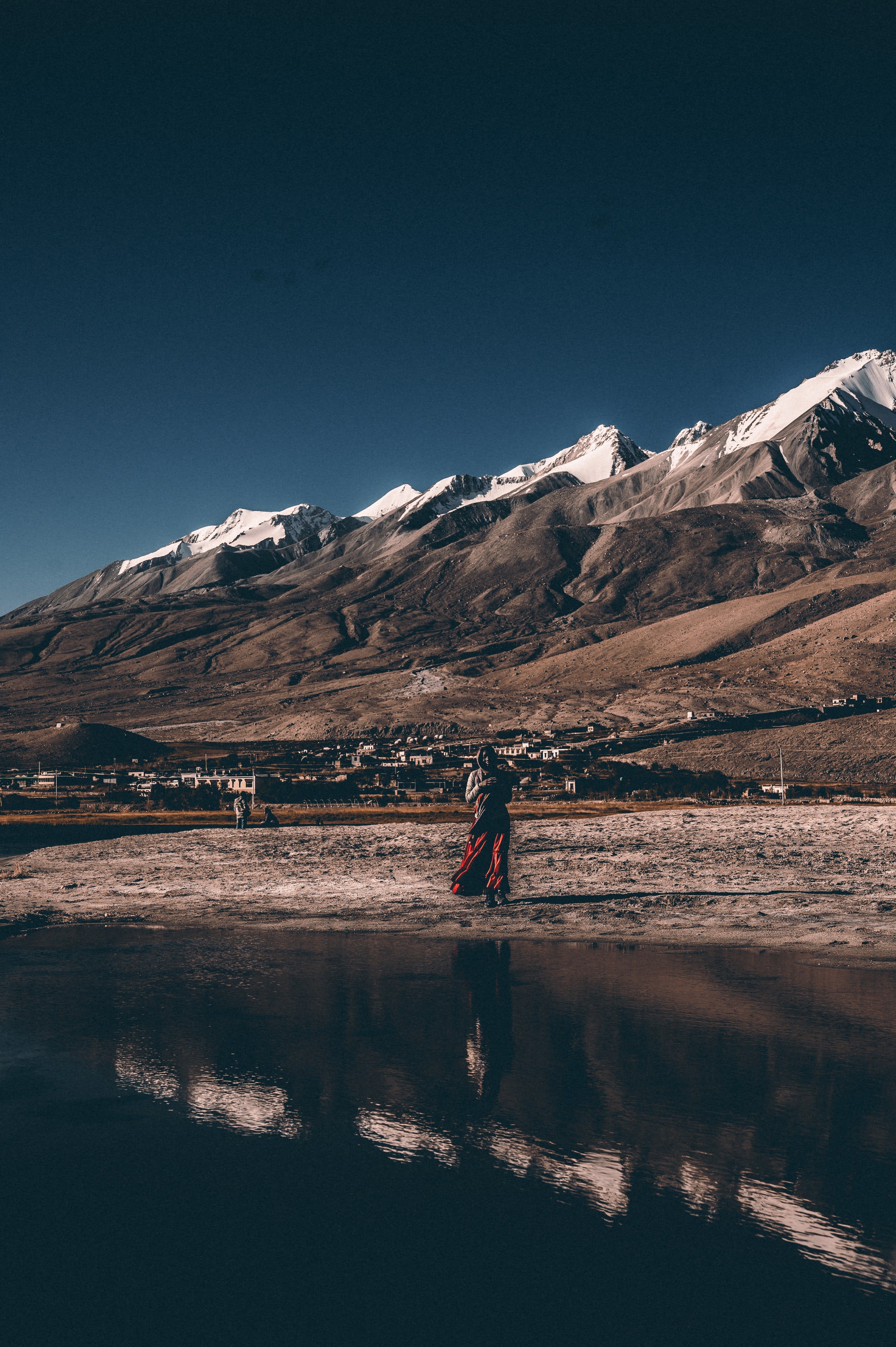 A person walking on a wet shore, reflected, snow peaks behind