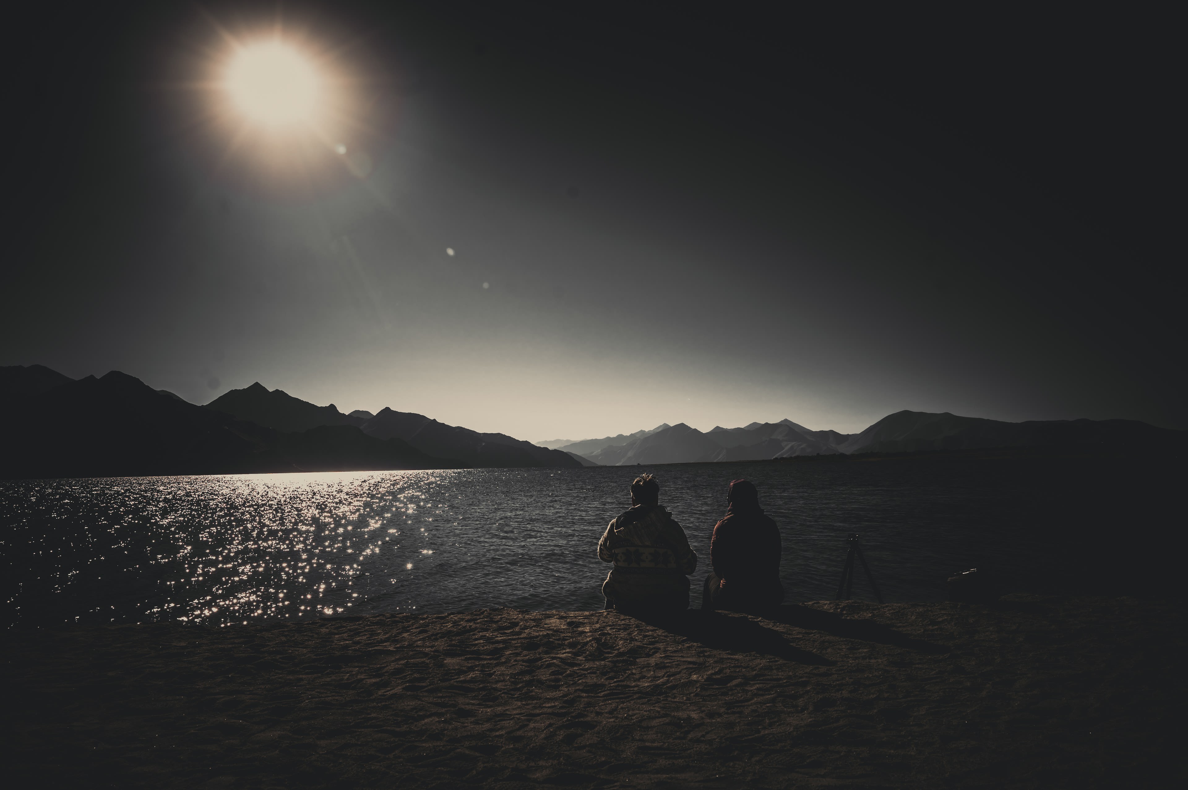 Two people sitting by a lake looking into low sun glare