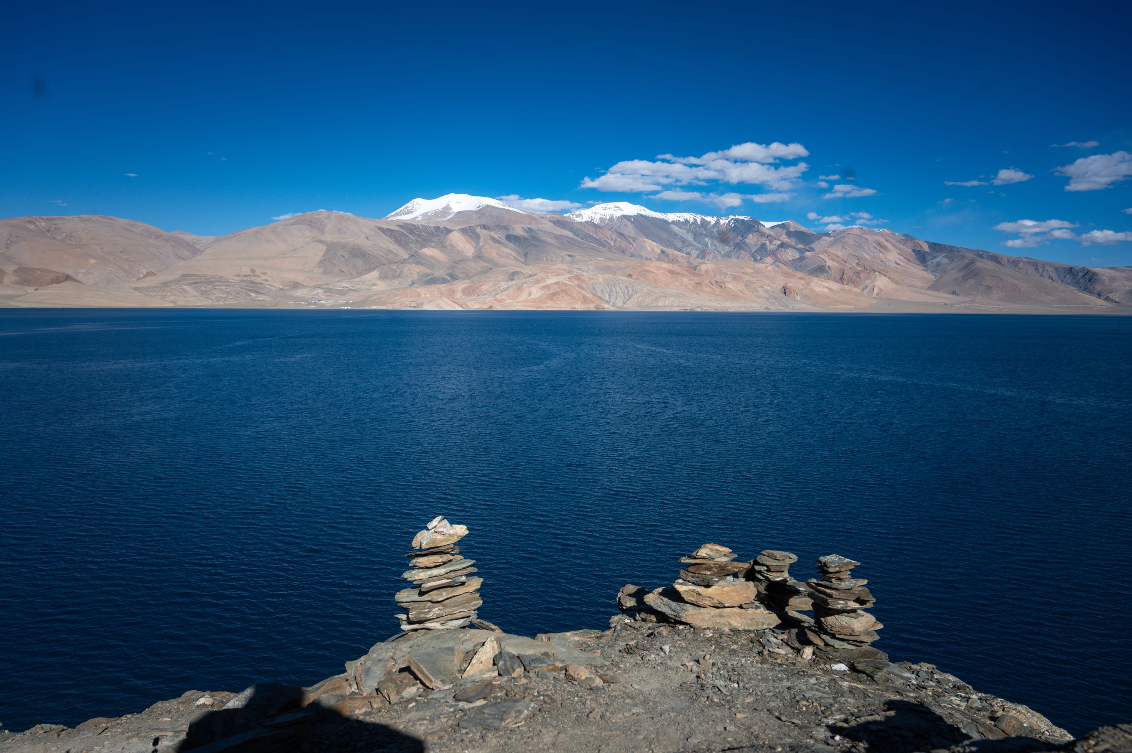 Stone cairns above a deep blue lake and tan mountains