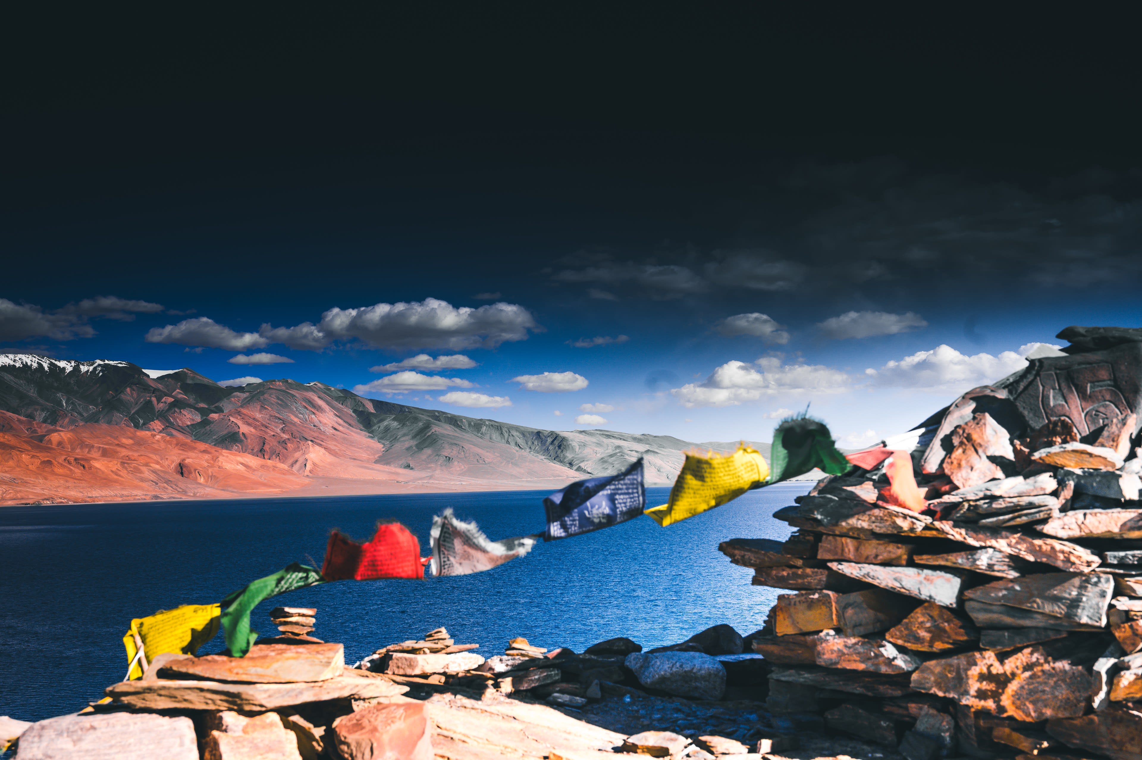 Carved mani stones and prayer flags beside a turquoise lake with red tents