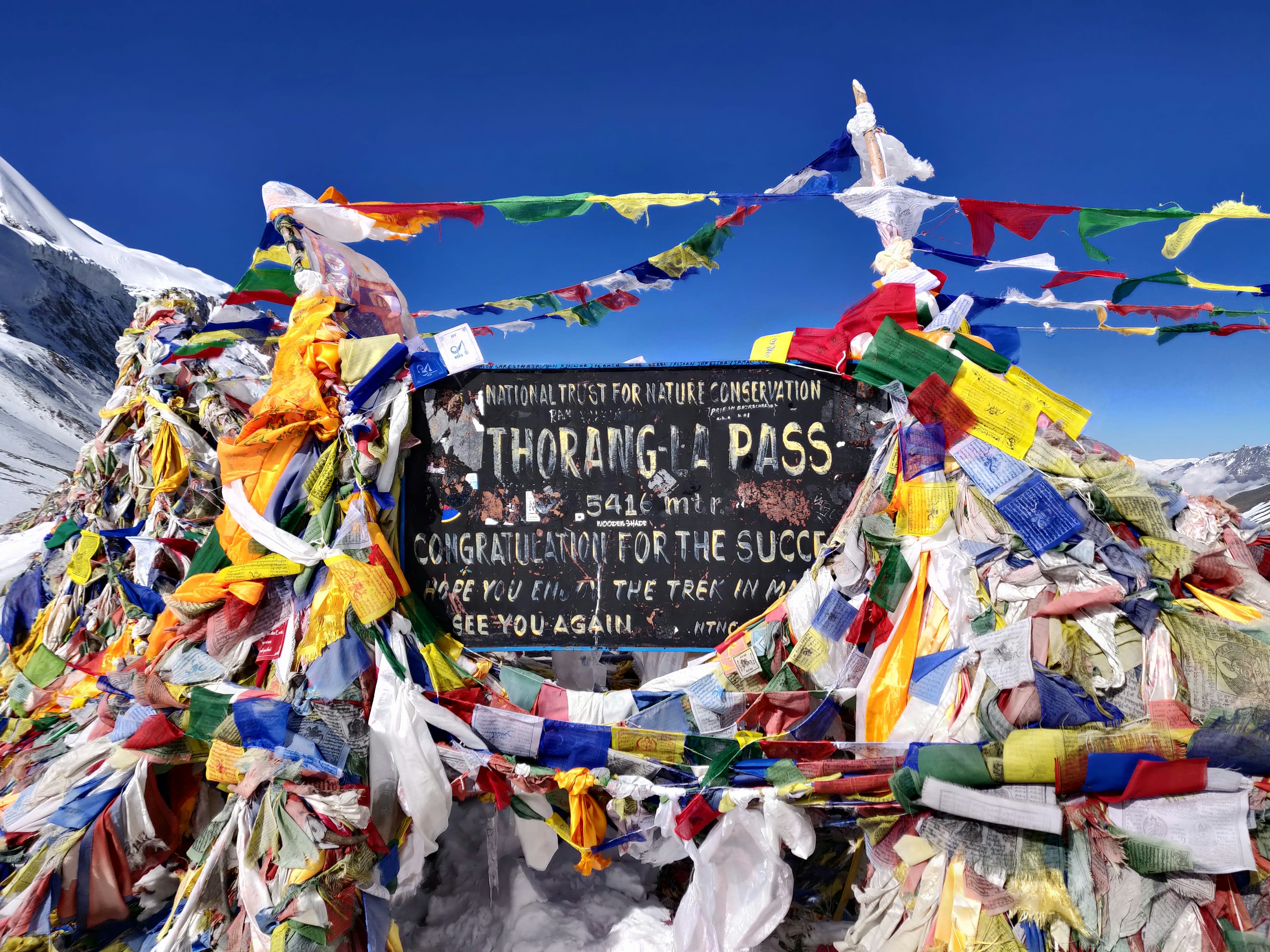 The Thorong La pass sign buried in colourful prayer flags