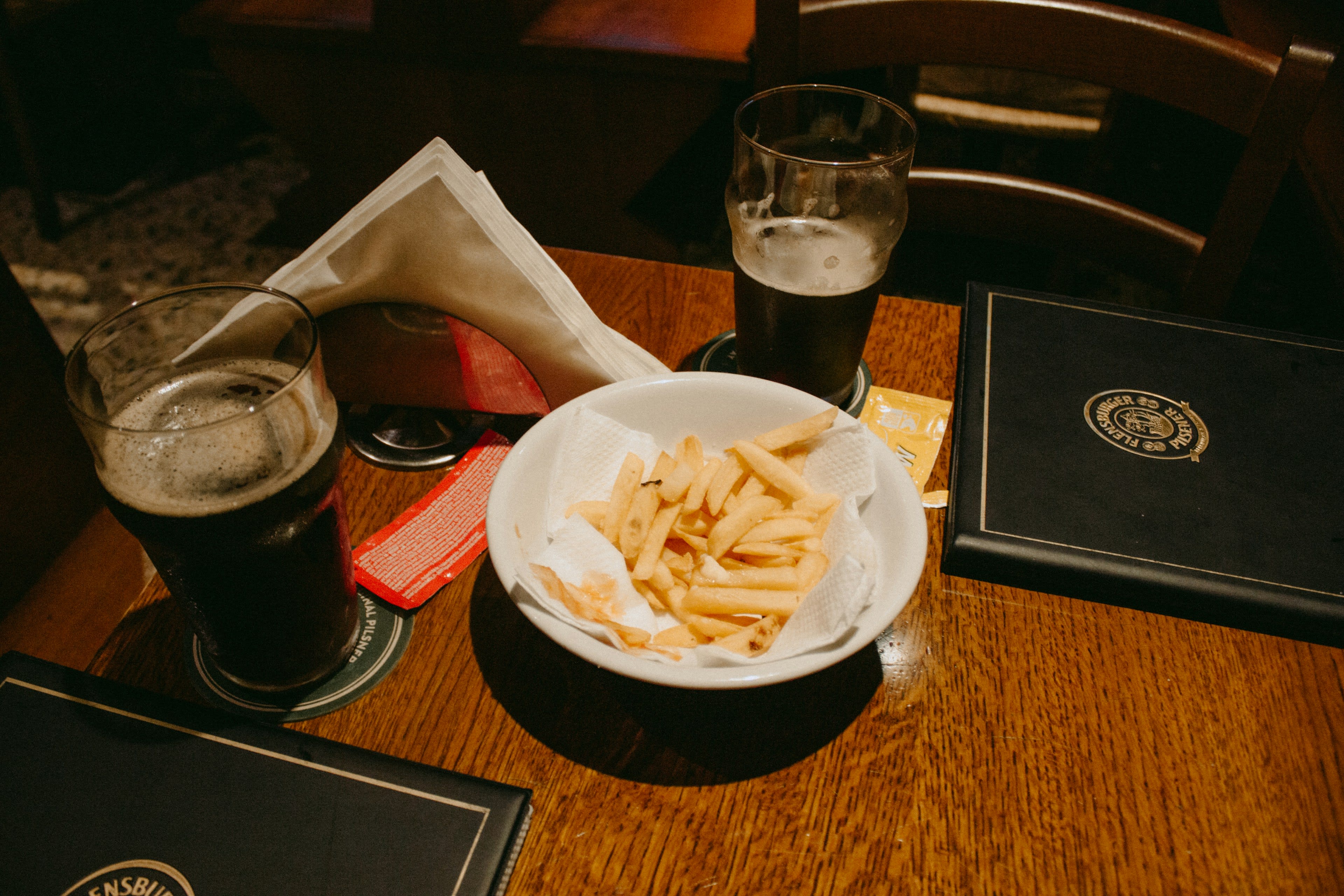 A bowl of chips and a dark pint on a wooden pub table