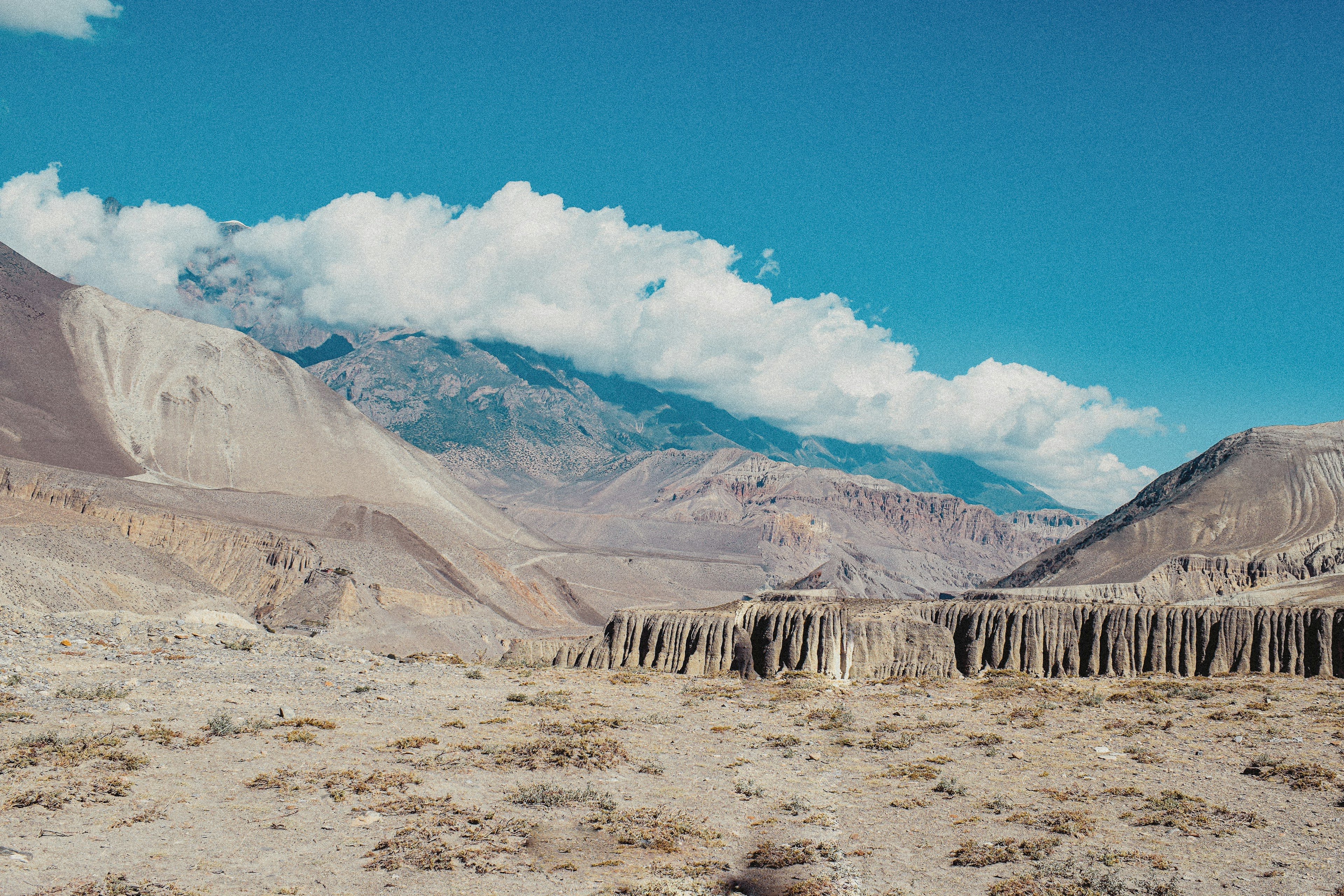A wide arid valley of banded cliffs and dry riverbed under a big sky