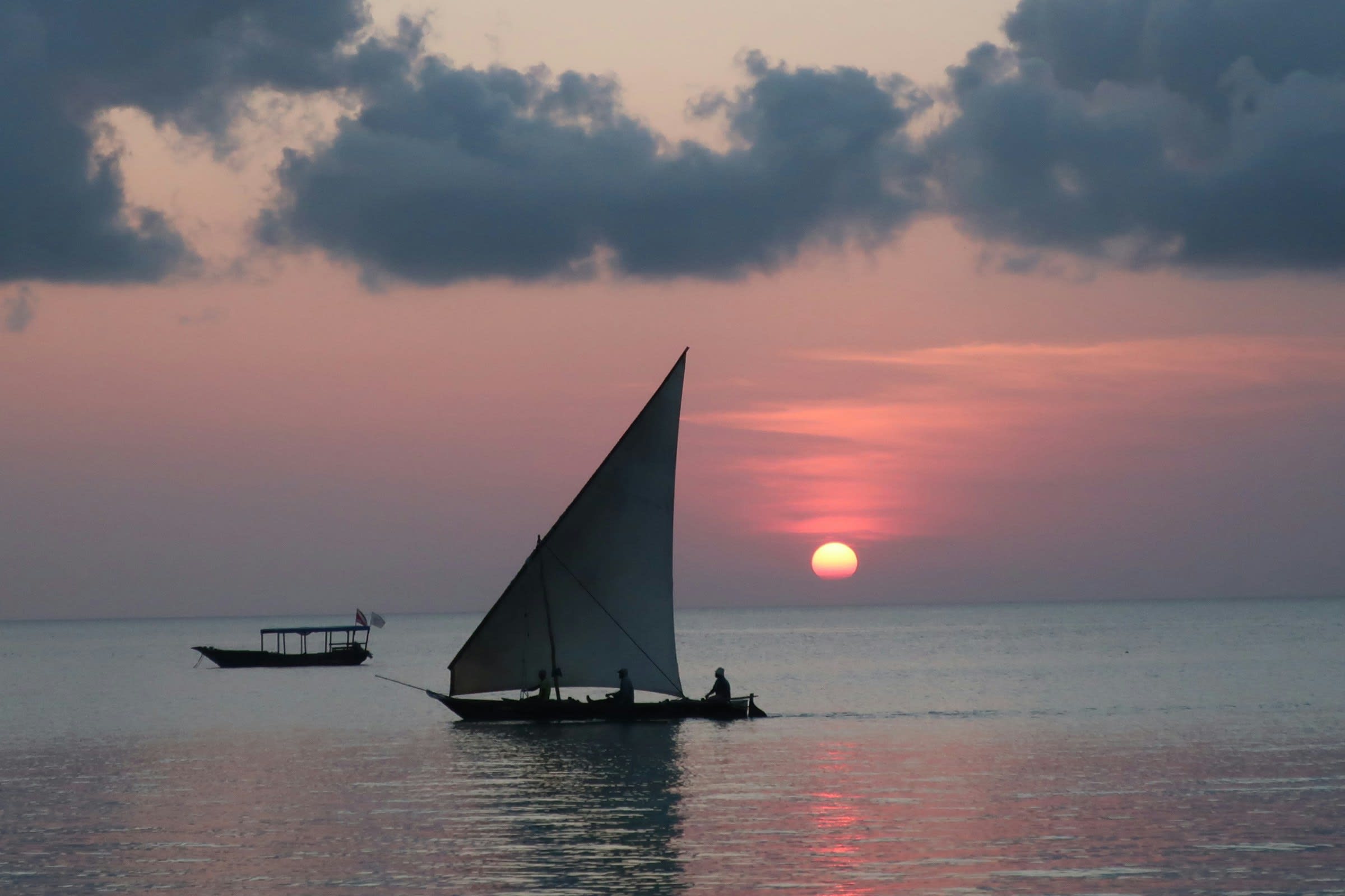 A dhow under sail crossing calm water at golden hour