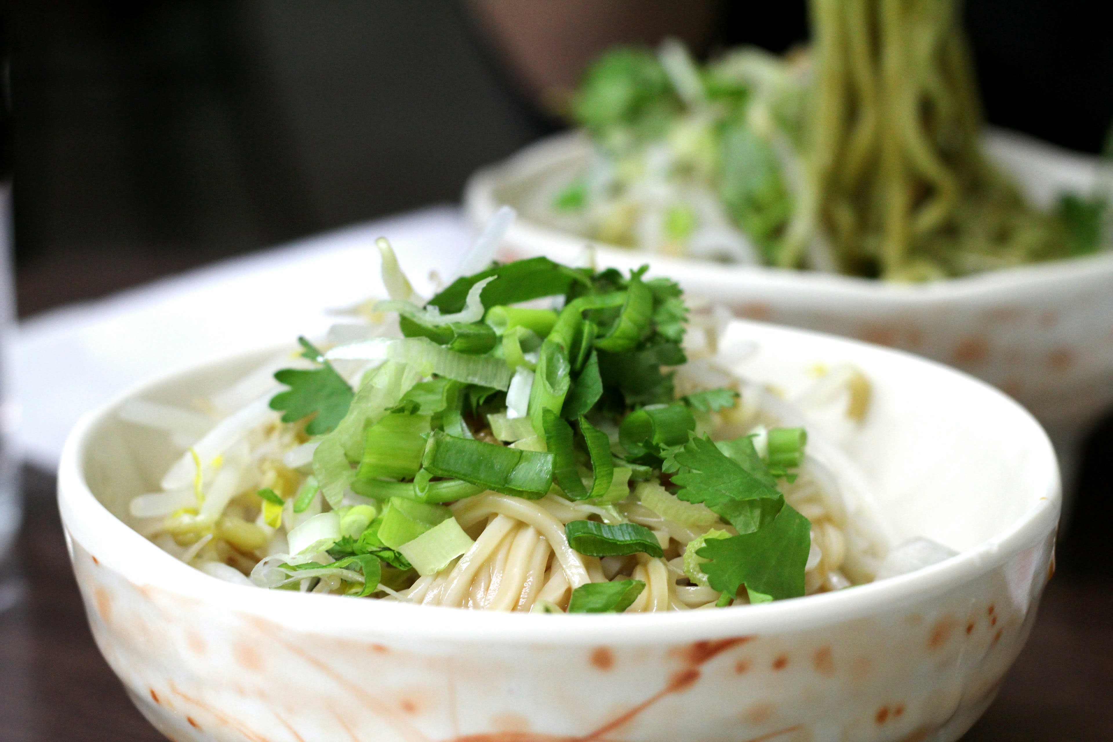 A bowl of noodle soup piled with fresh coriander on a counter