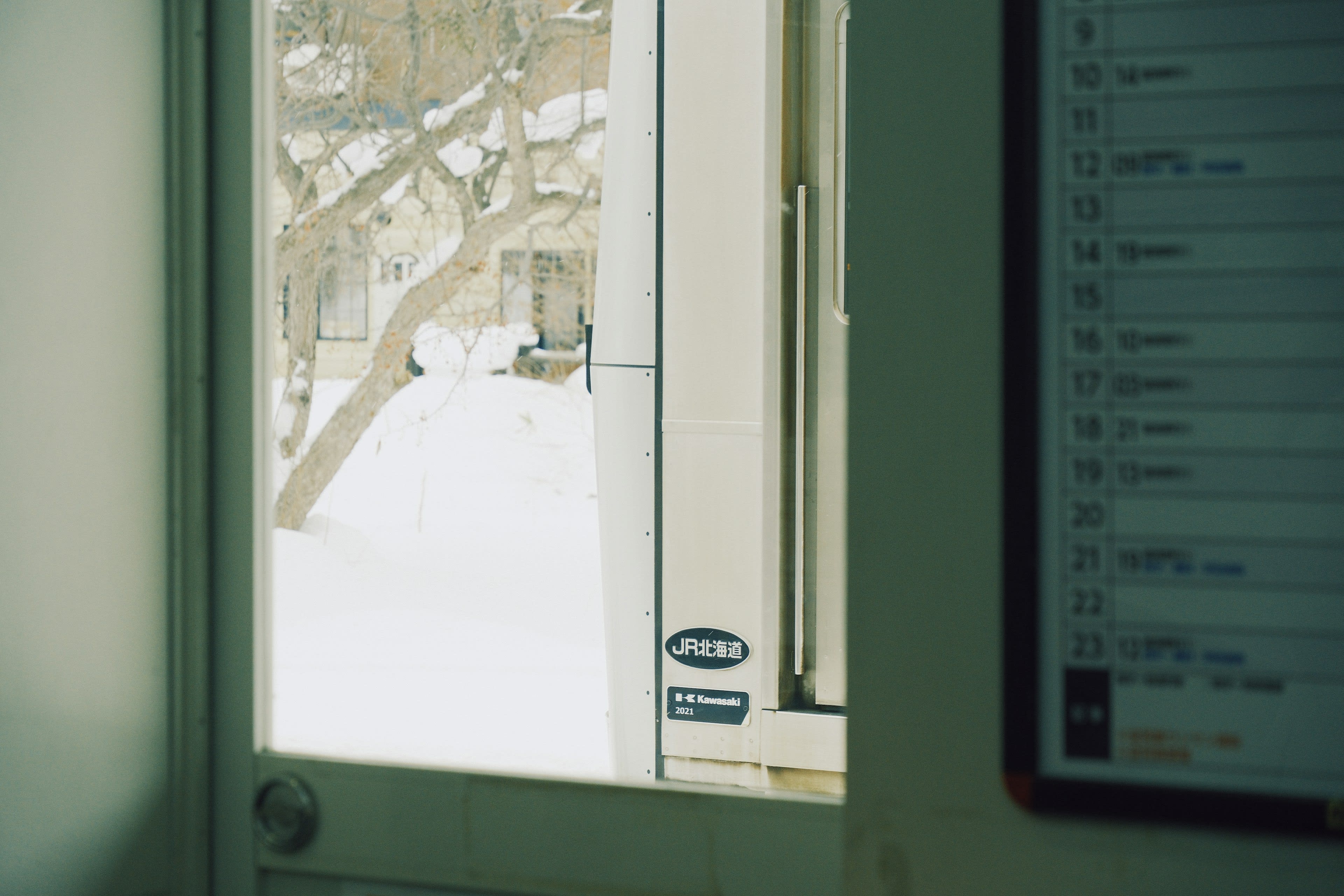 Snowy fields seen through a local train window with a small calendar hanging beside it