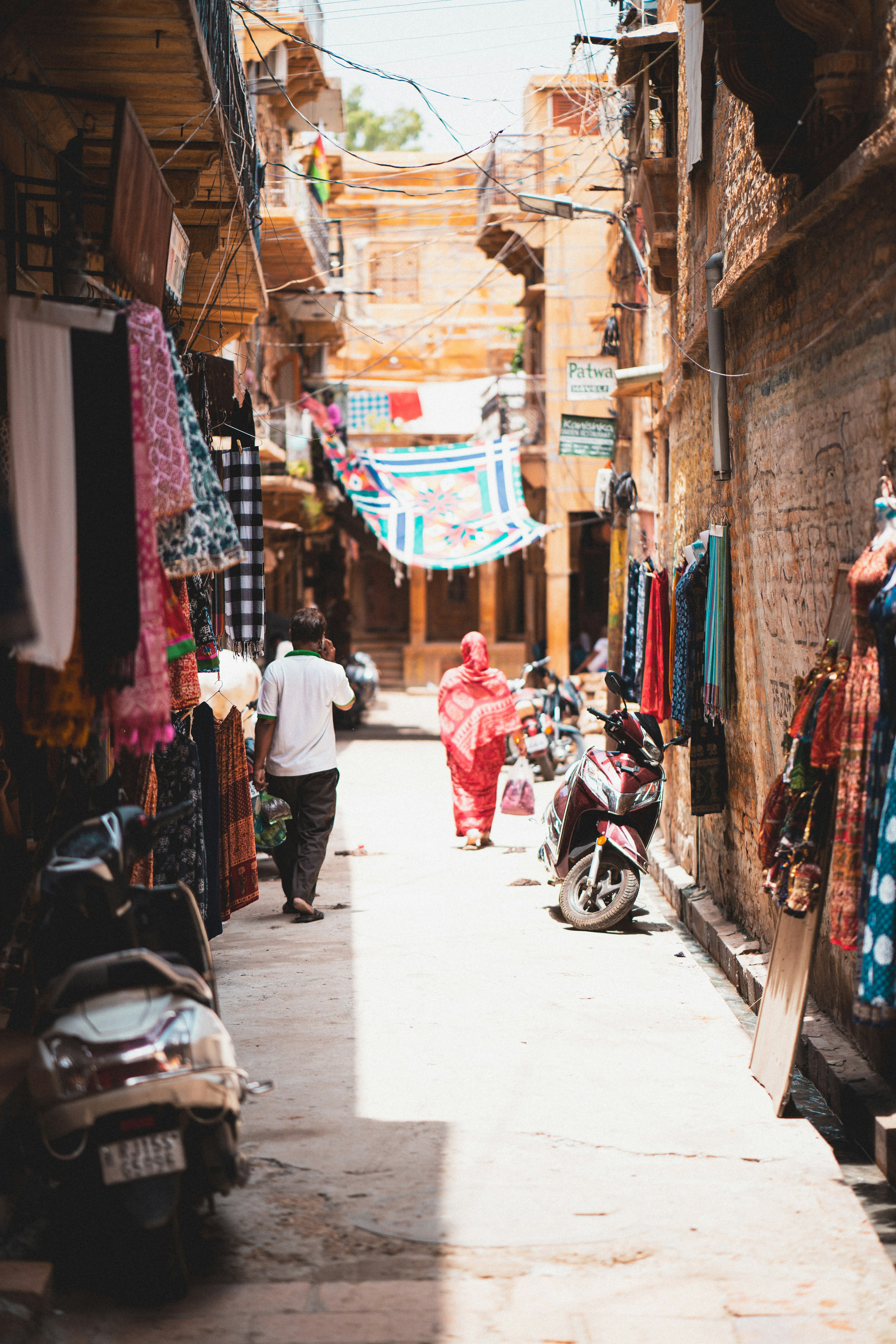 A man walking down a narrow golden sandstone lane past a parked motorcycle