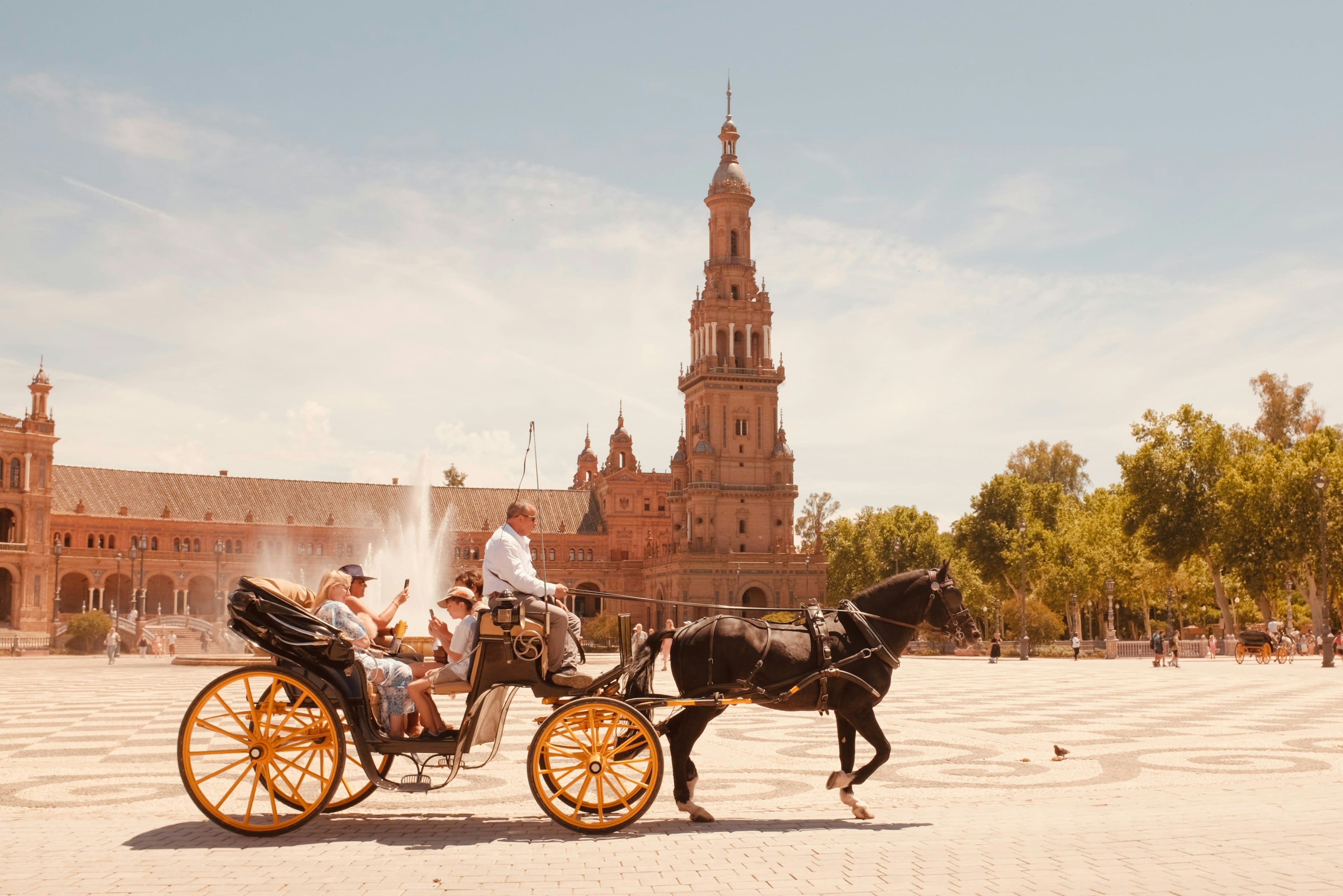 A horse-drawn carriage crossing the wide plaza before a tiled tower
