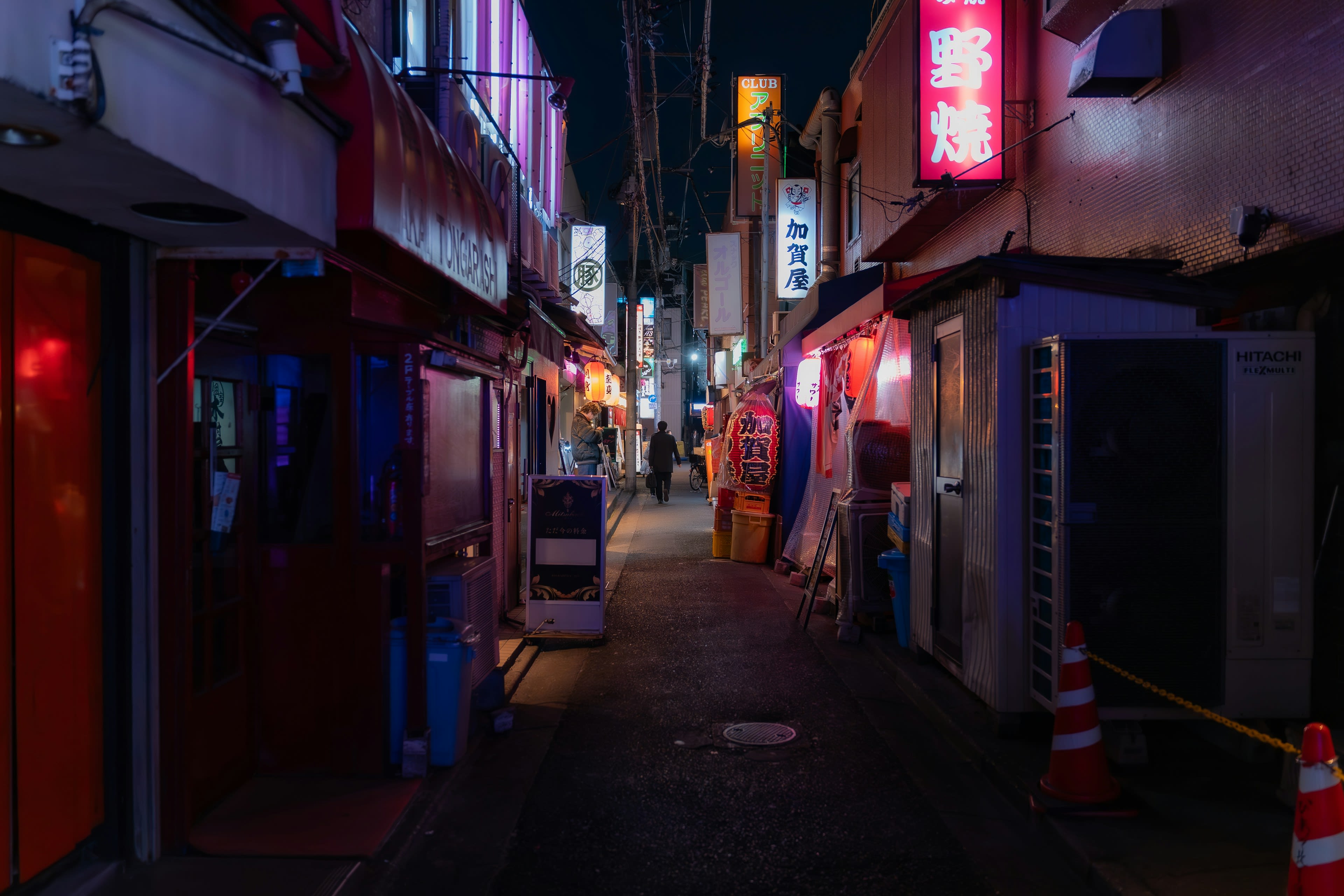 A narrow alley at night lined with tiny bars and glowing neon signage
