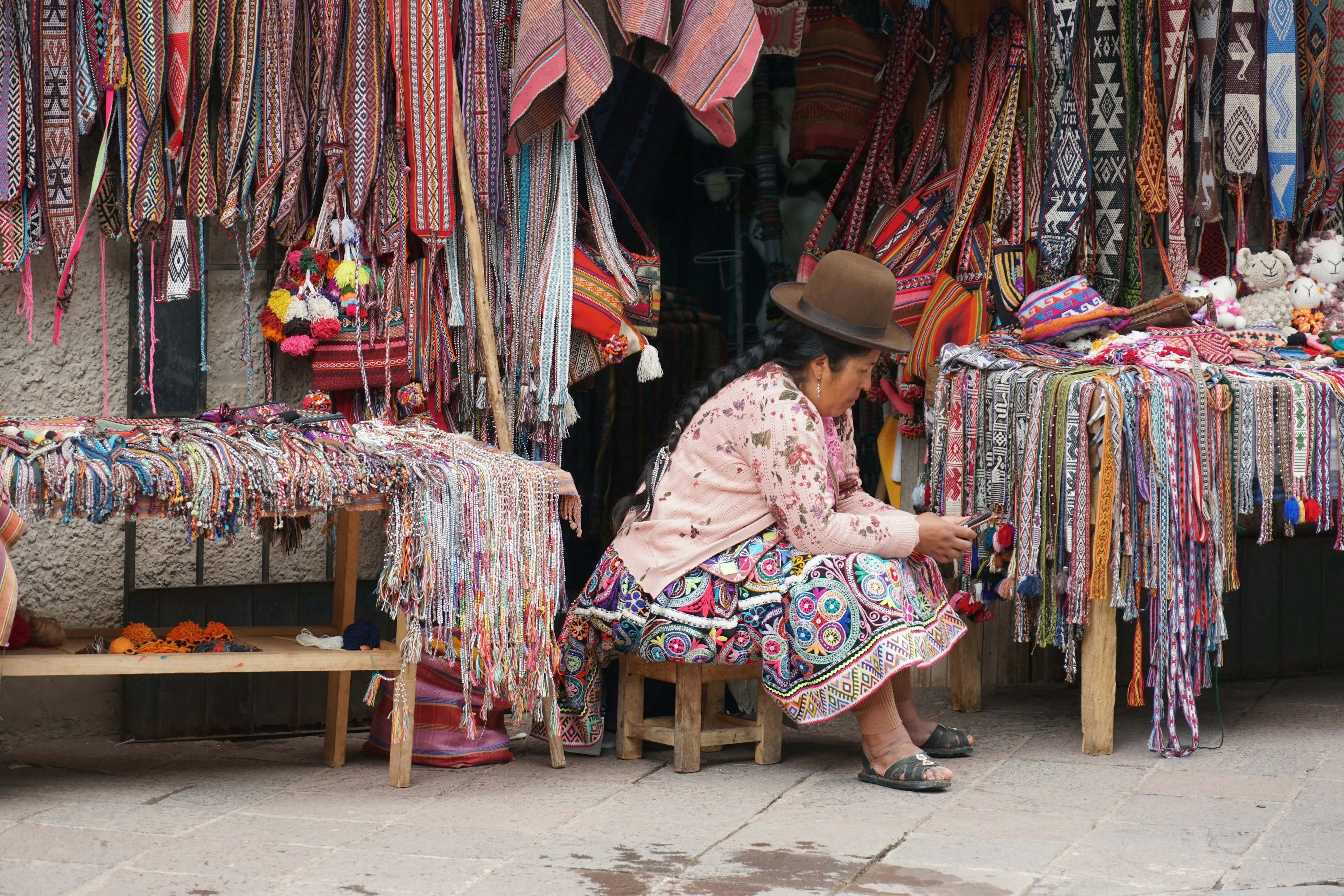 A woman at a market stall hung with brightly woven textiles