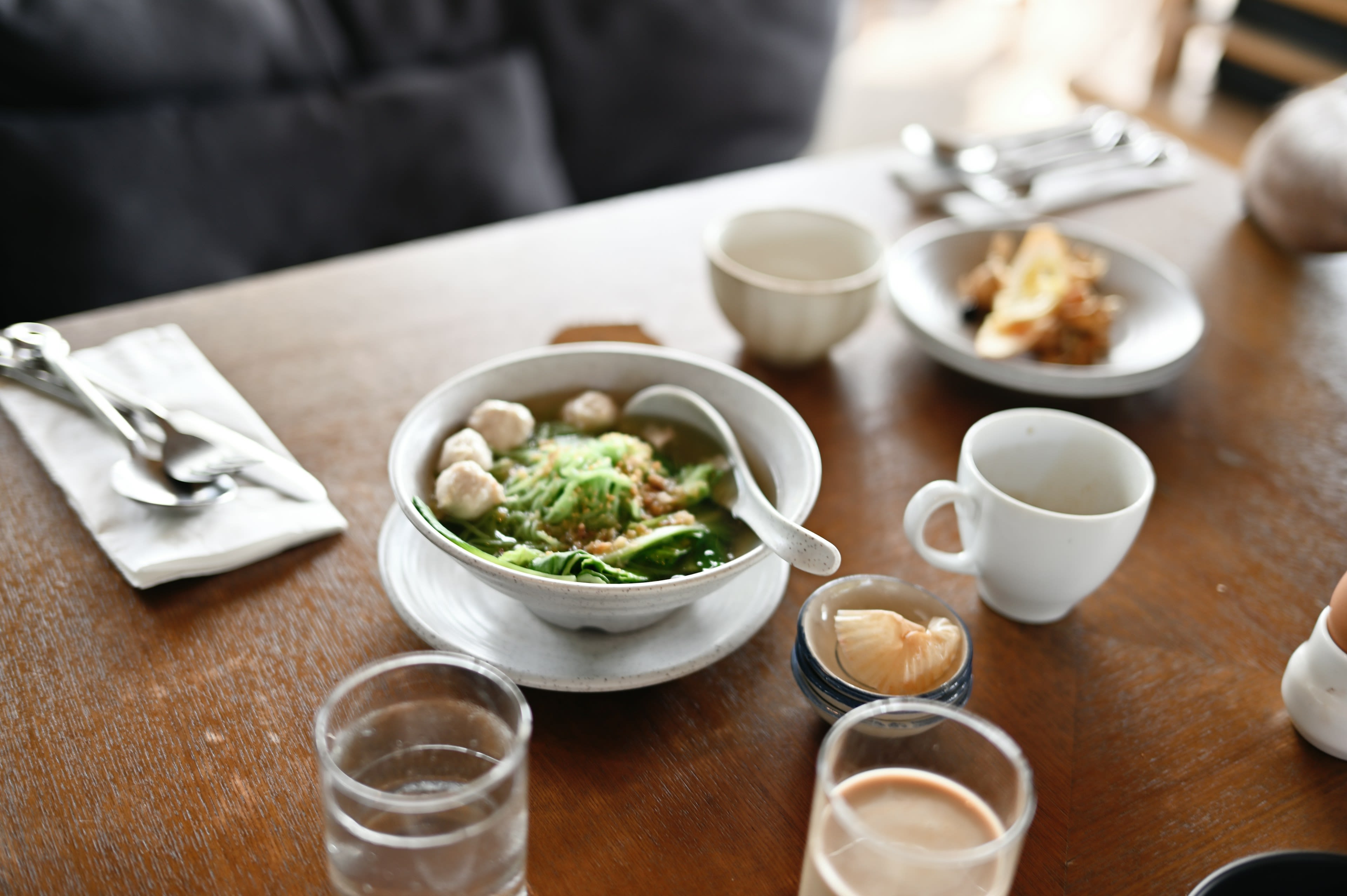 A bowl of soup, small side plates and a cup of coffee on a wooden café table