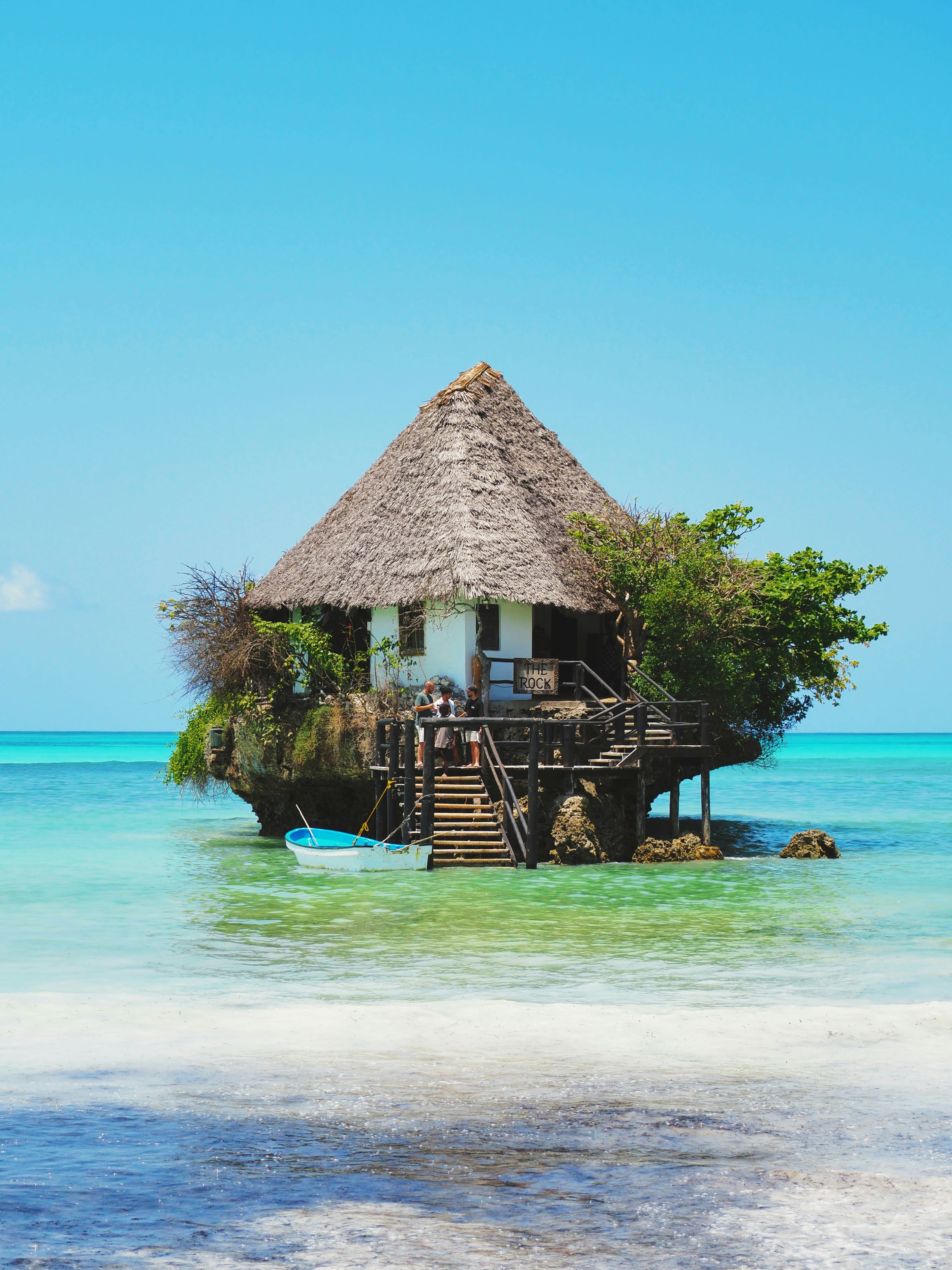 A thatched restaurant standing on a small coral rock in shallow turquoise sea