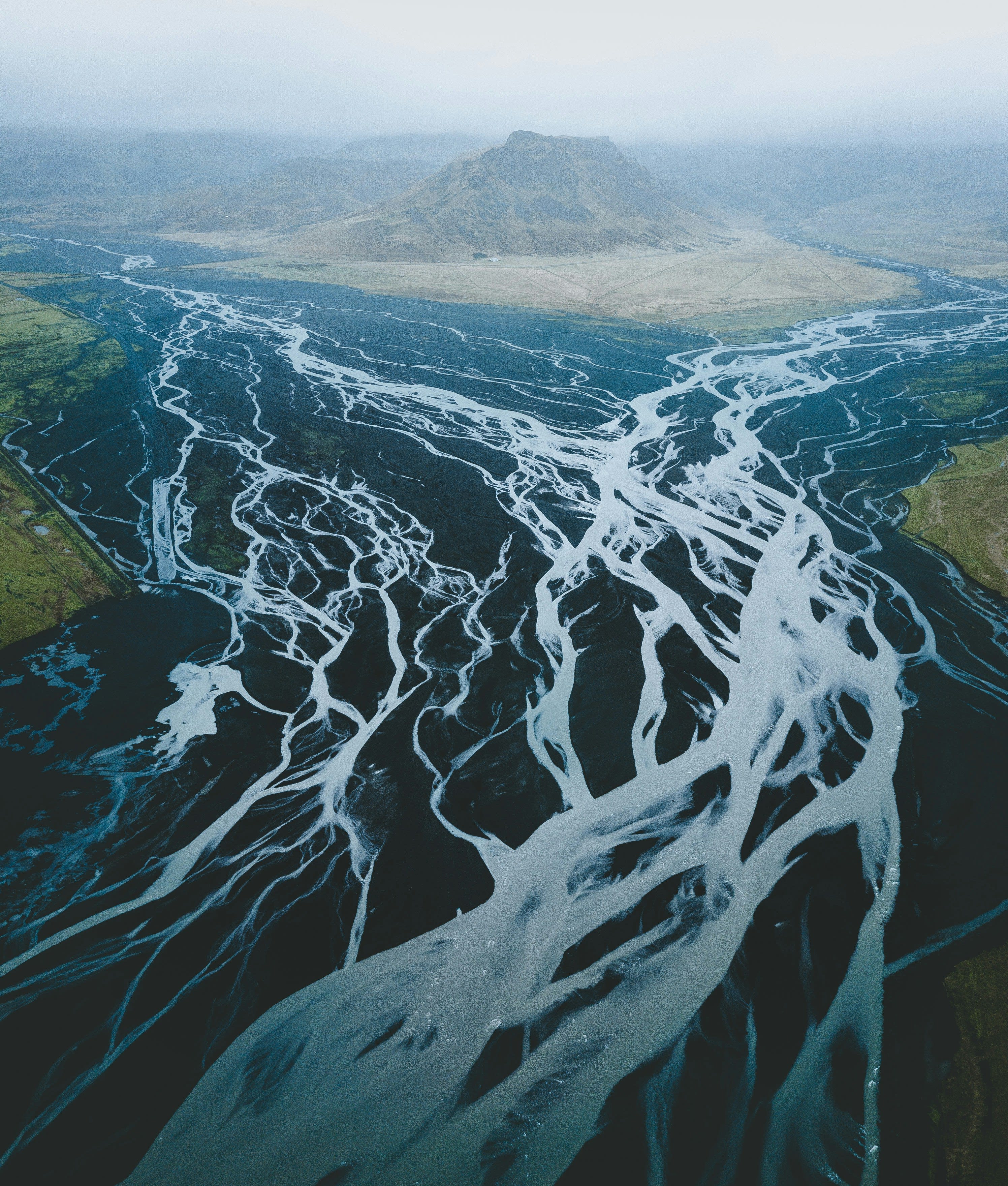 Top-down aerial view of white glacial meltwater braiding through dark sand