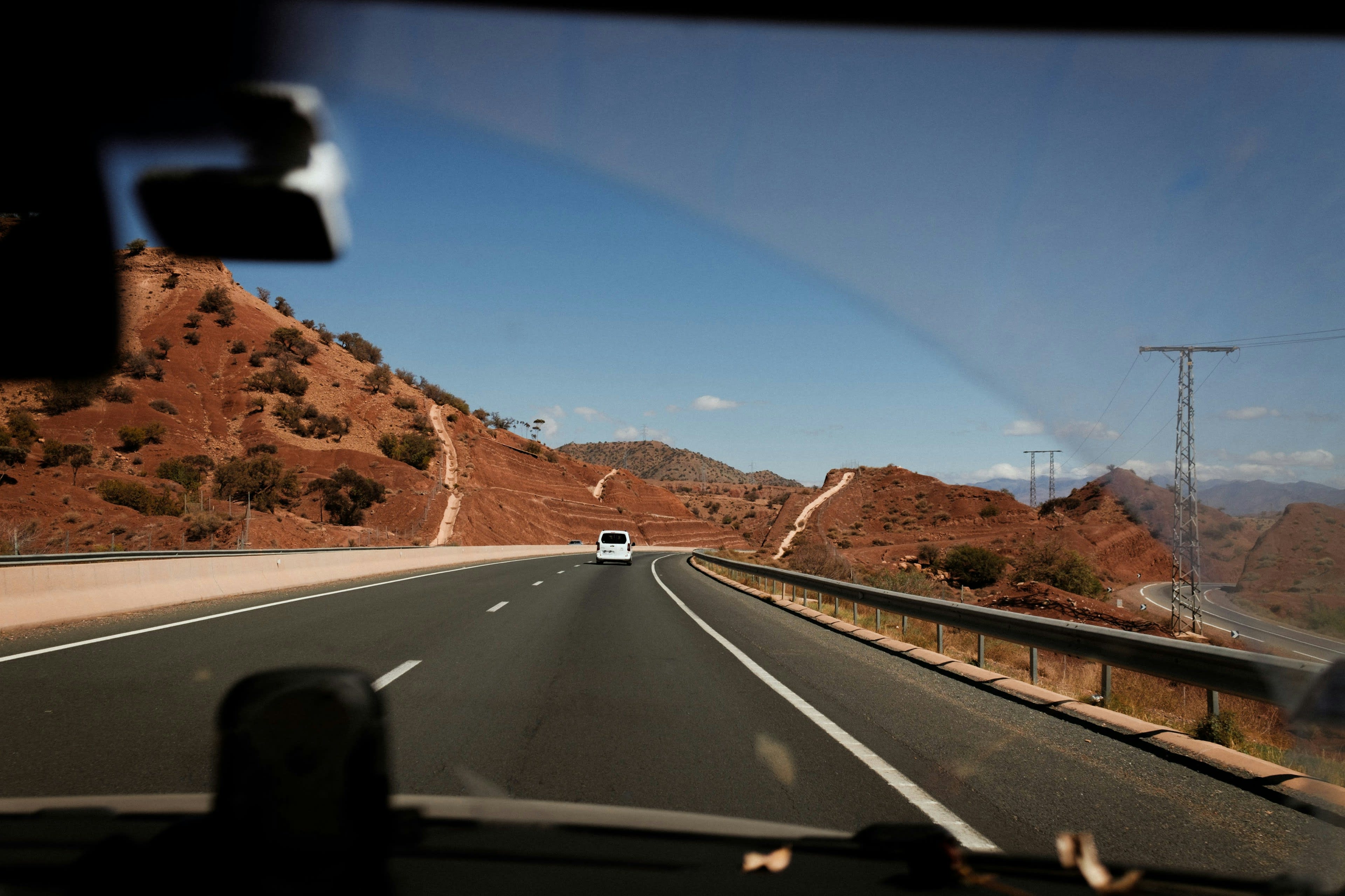 A road curving through red and brown mountains seen from inside a moving car