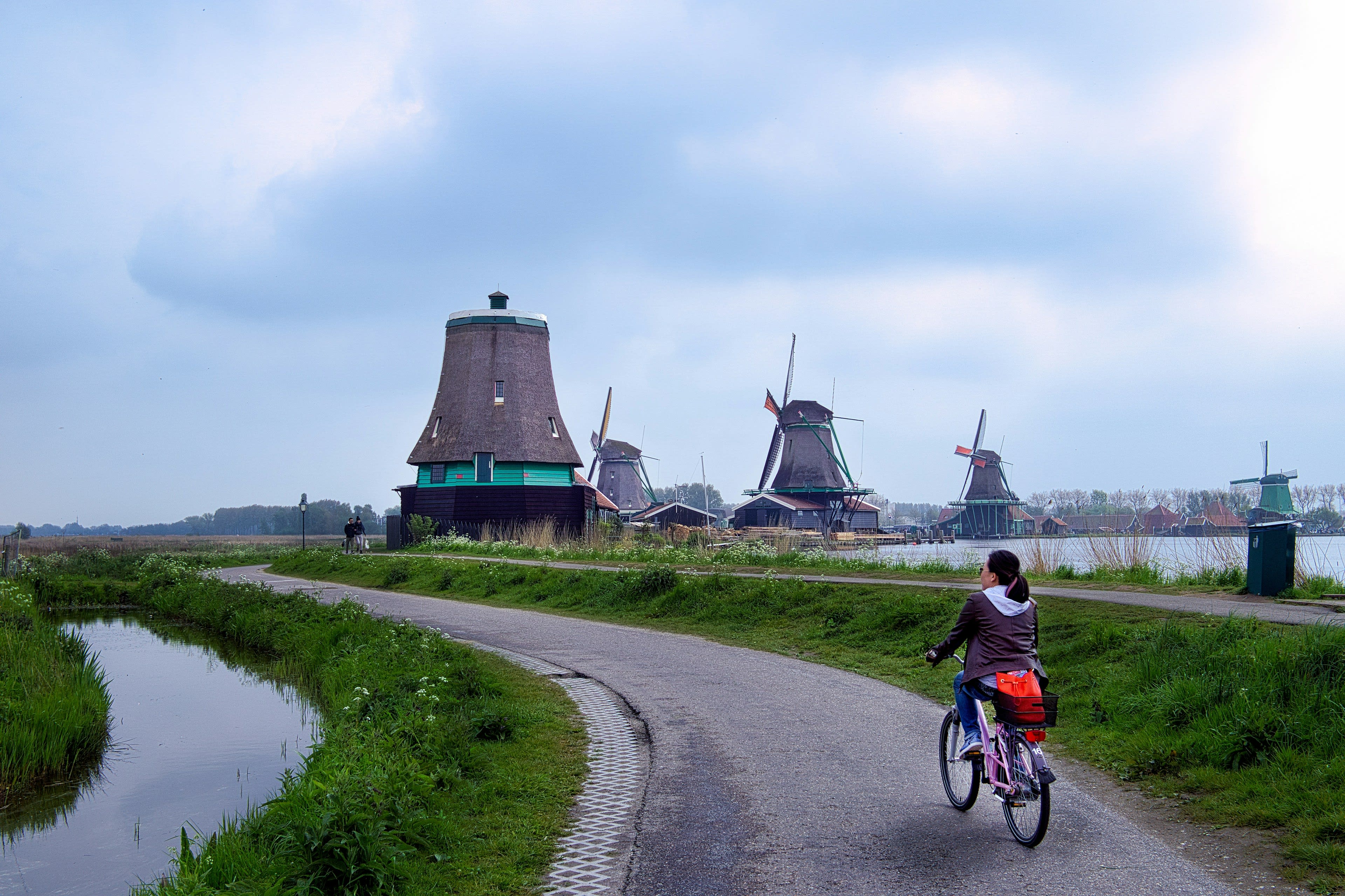 A cyclist riding a path toward old Dutch windmills along the water