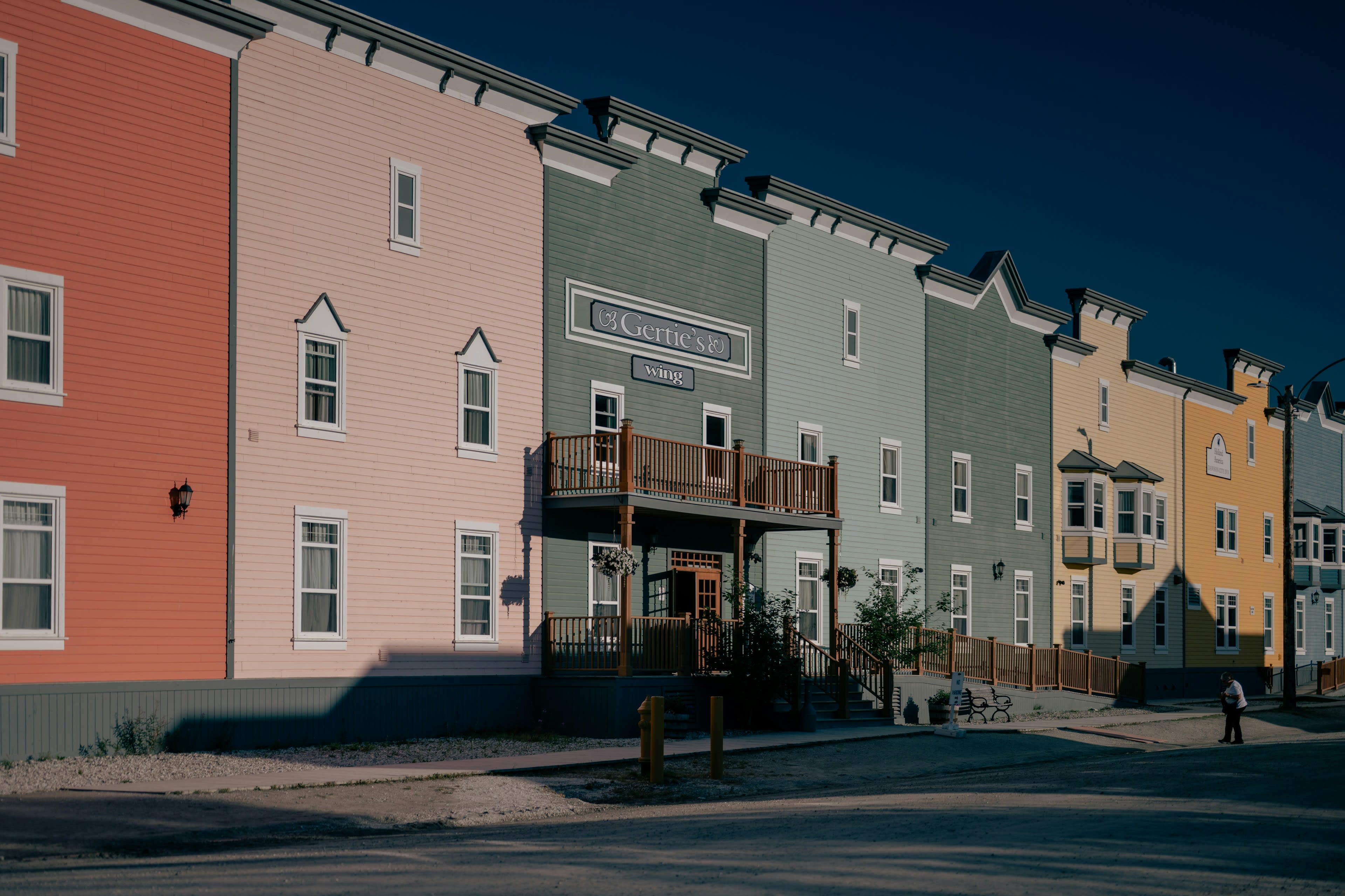 Colourful false-front wooden buildings along a quiet Dawson City street in sunlight