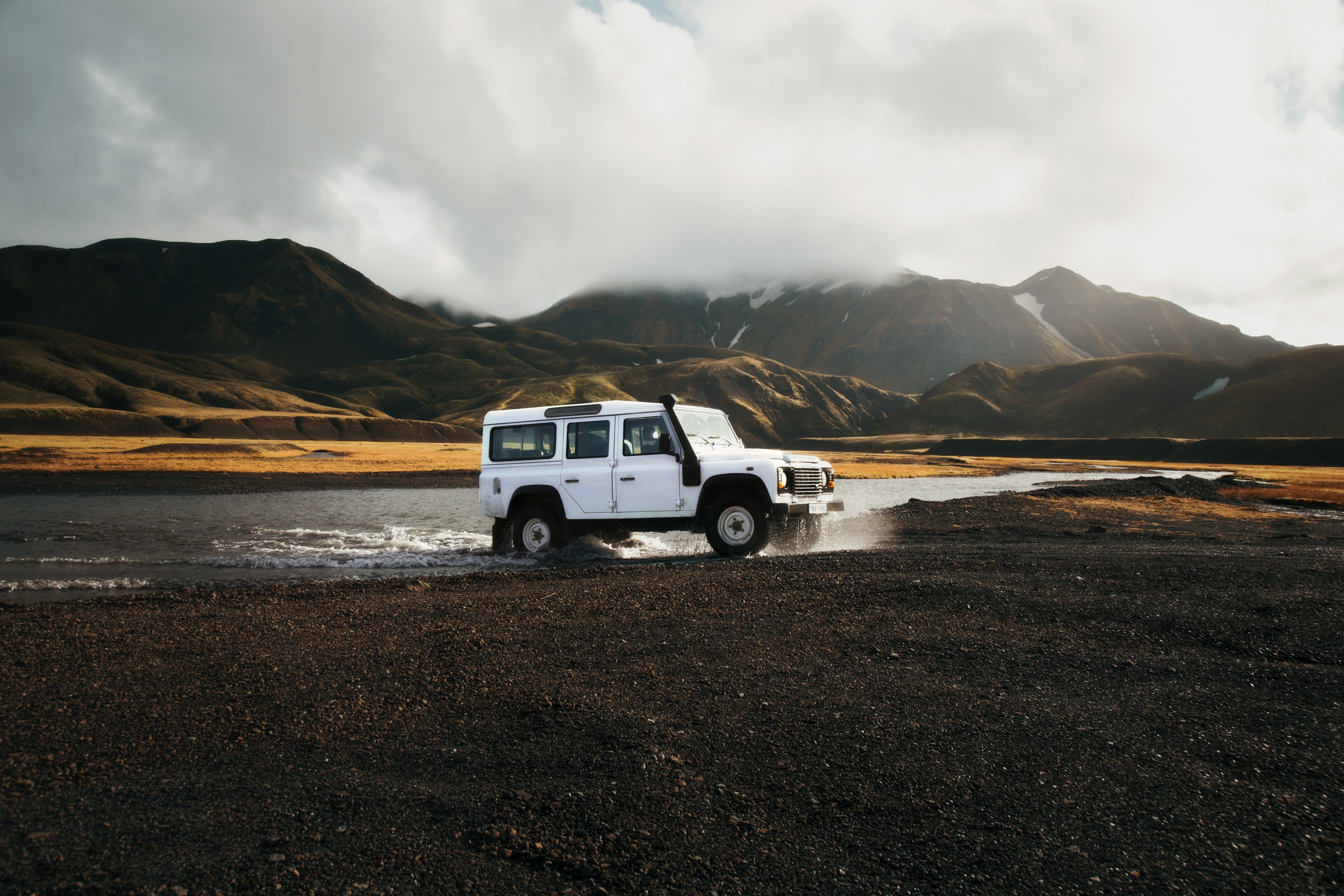 A white 4x4 crossing a highland river, water pushing around its wheels