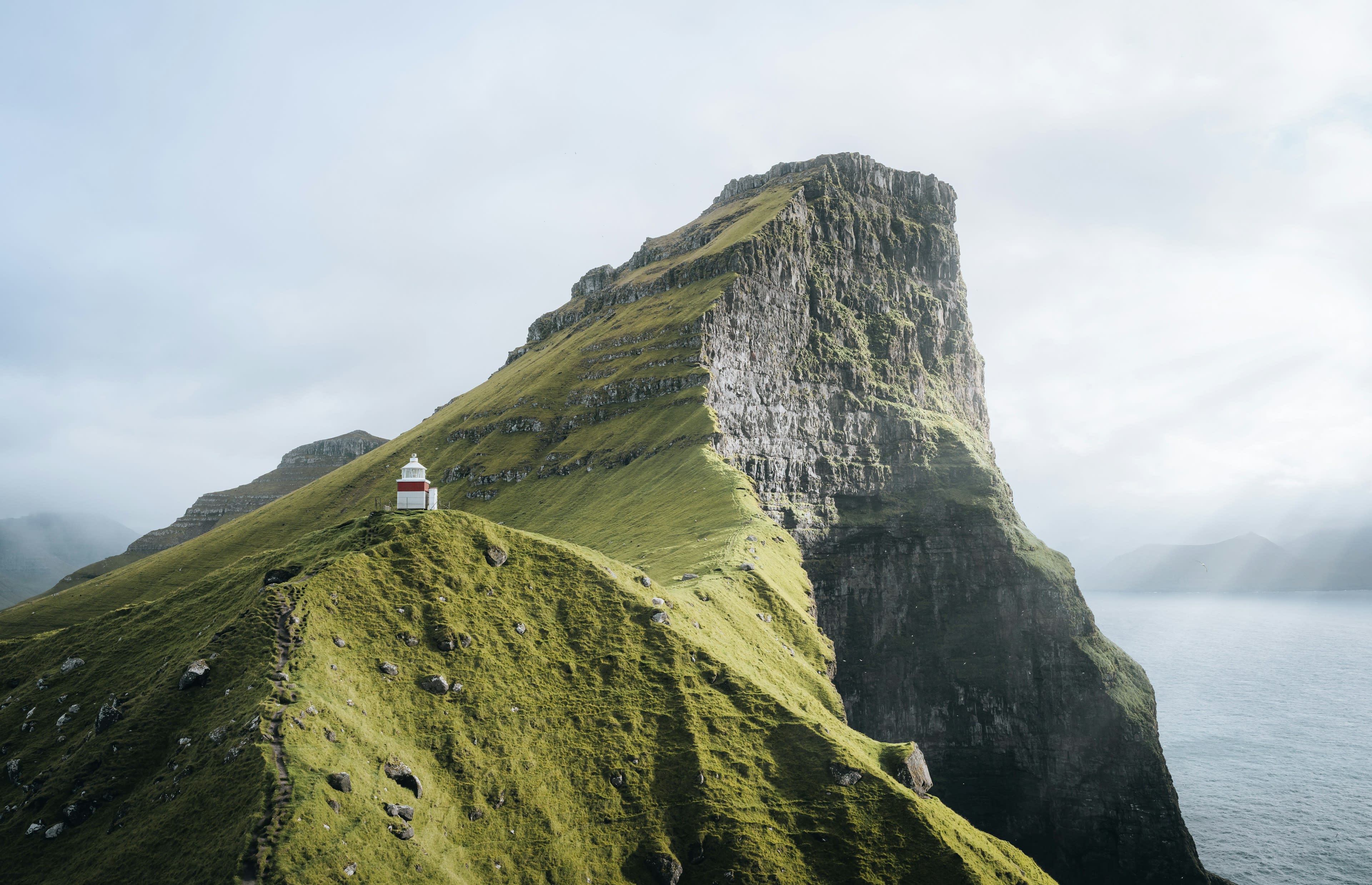 A small white lighthouse on a narrow green ridge above the sea