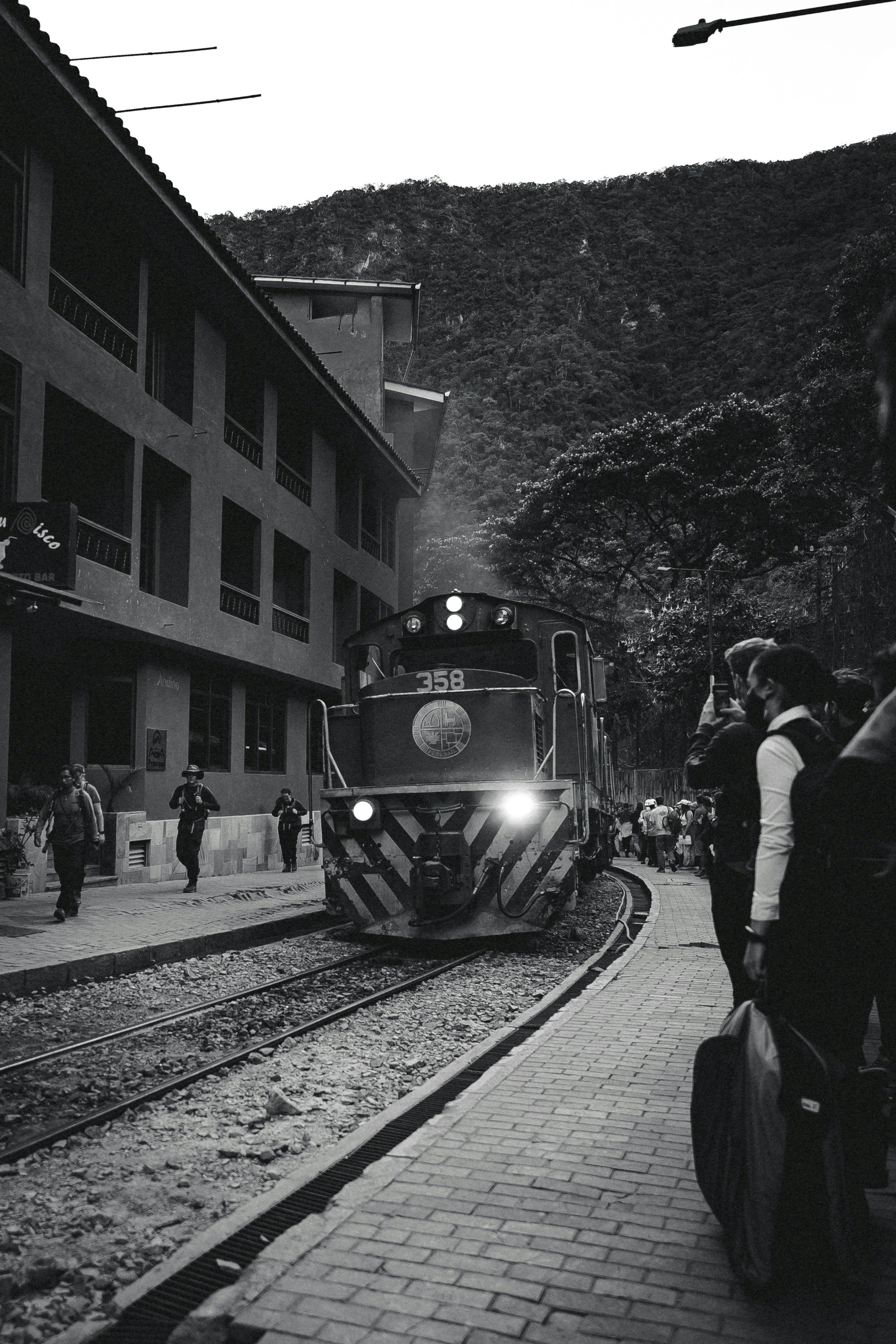 A train arriving through a narrow valley street in black and white