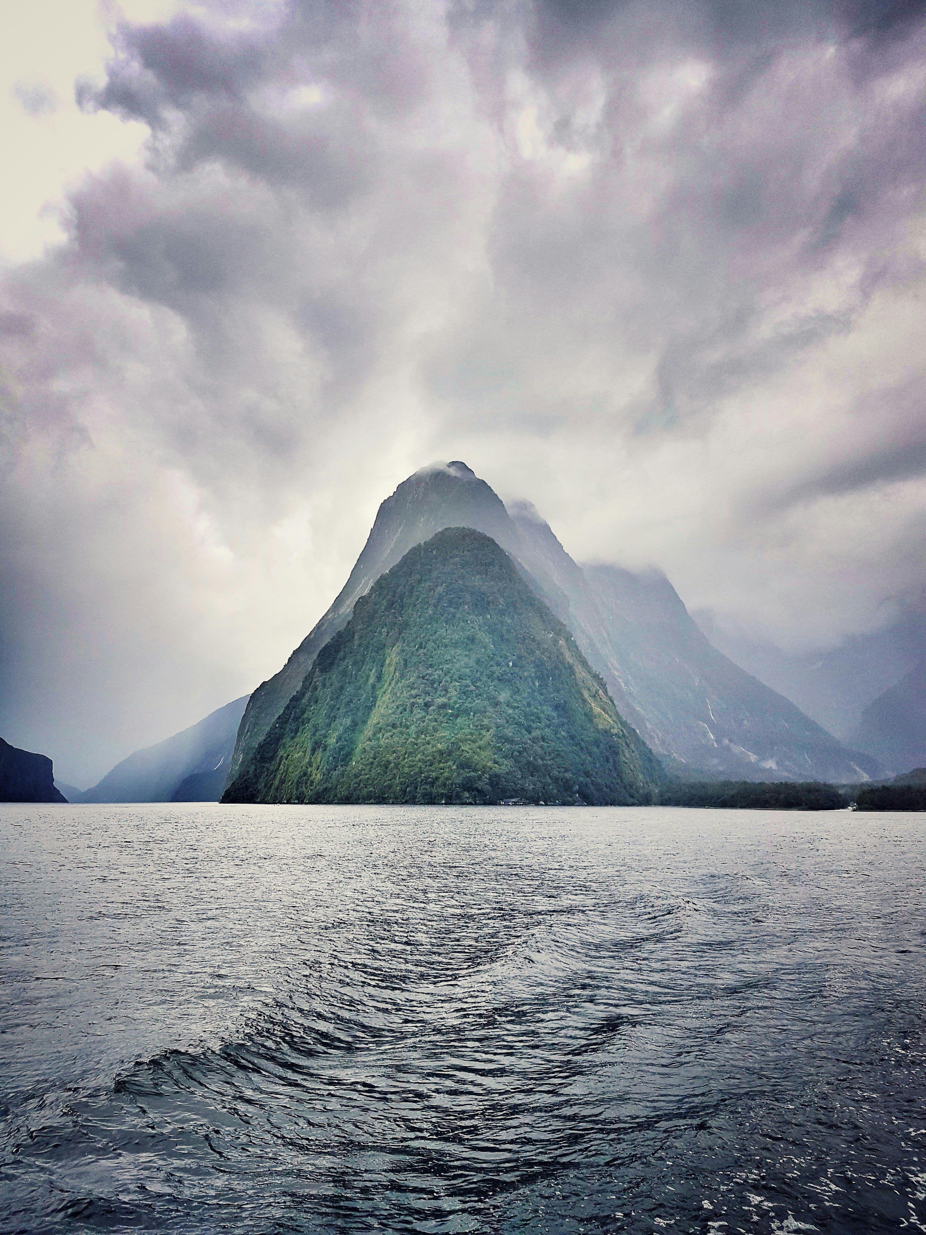A dark pyramid-shaped peak rising from a fjord under heavy cloud