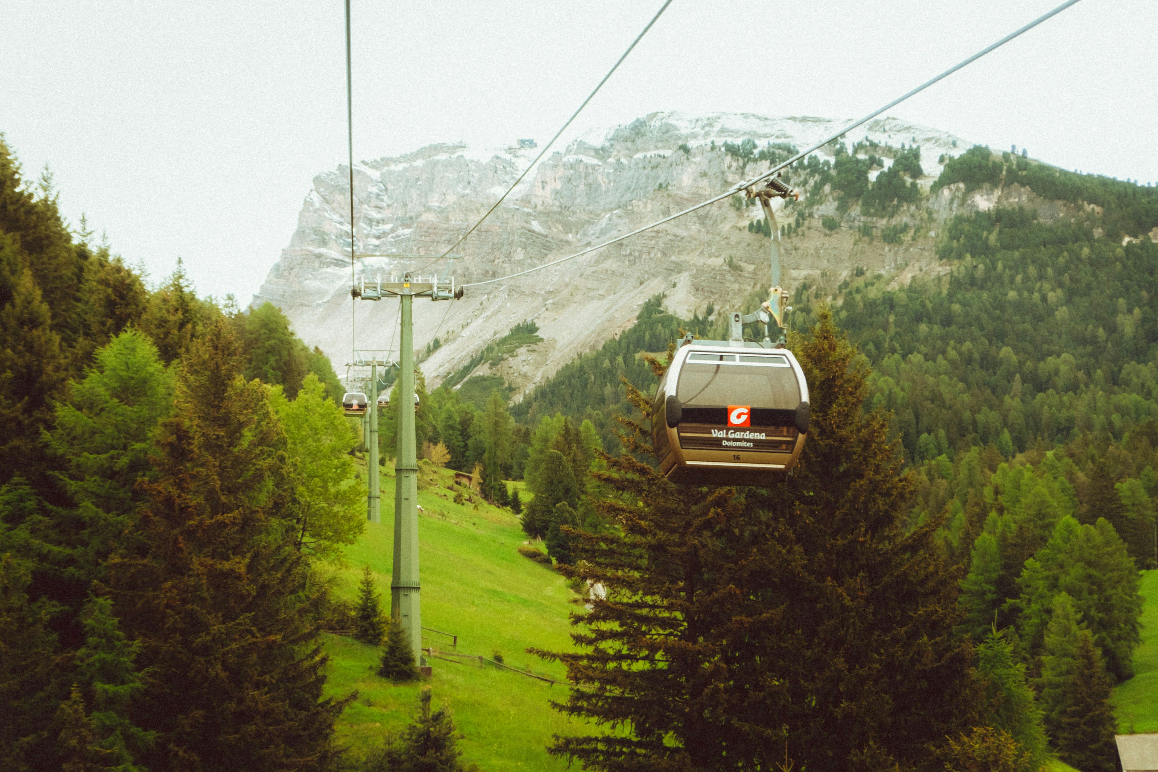A chairlift rising over steep green pasture towards grey peaks