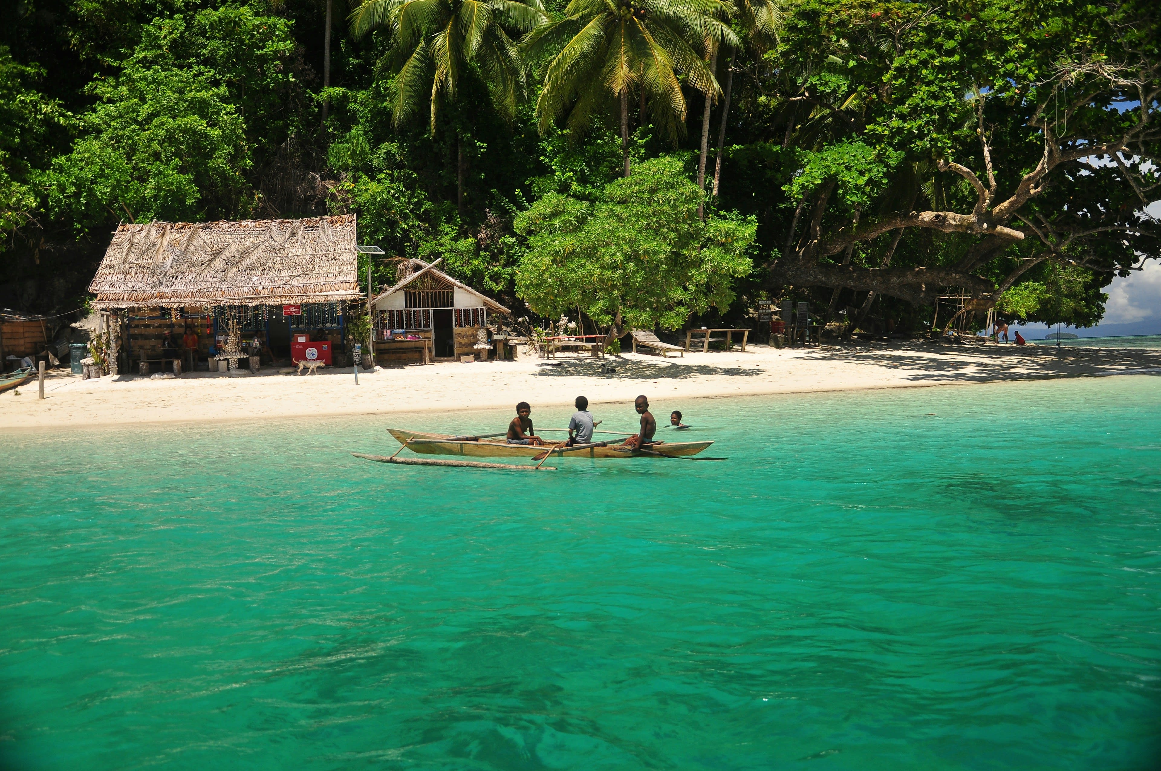 Children paddling a small boat in shallow turquoise water off a beach
