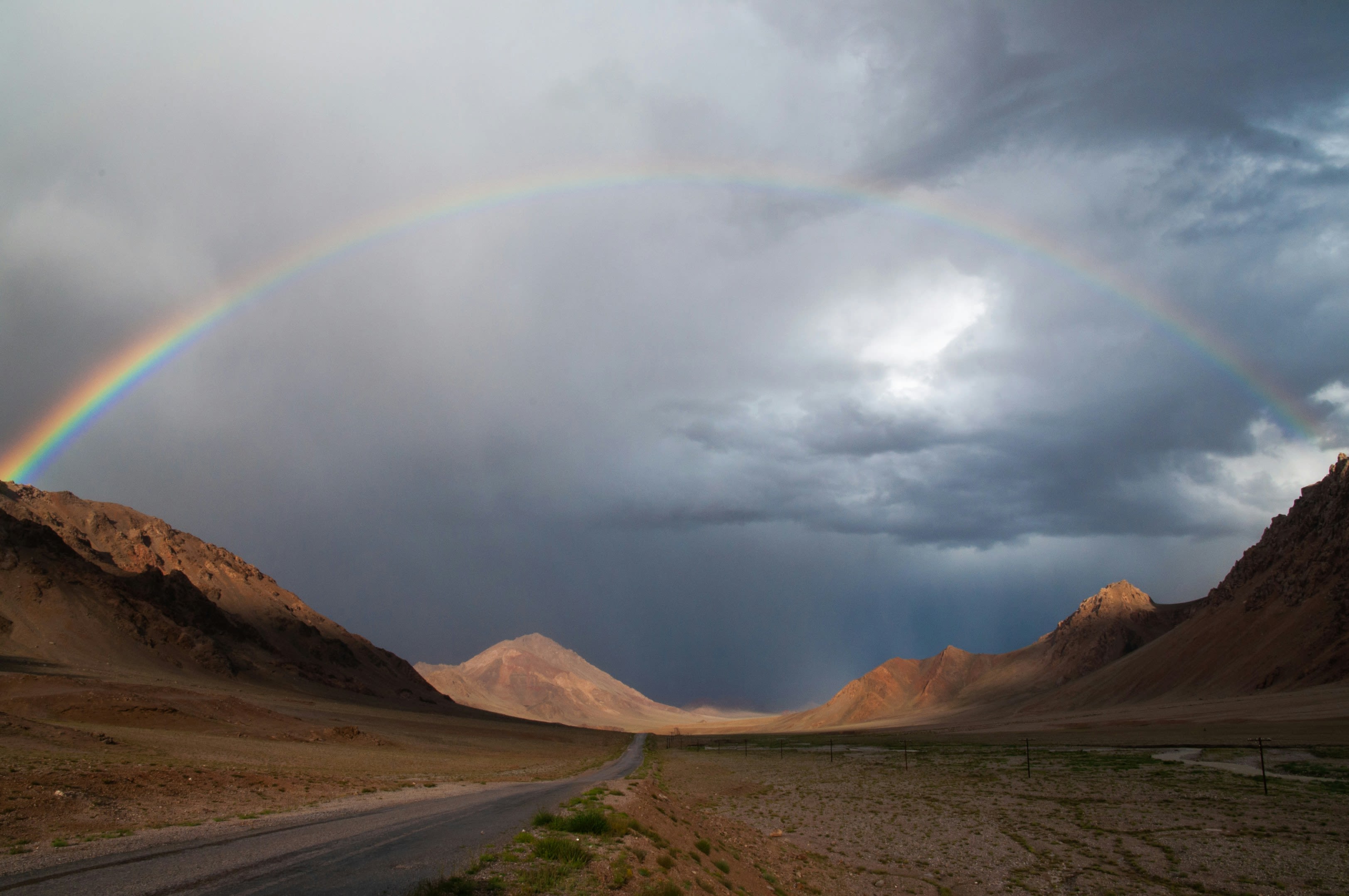 A rainbow over a dry mountain valley under a dark sky
