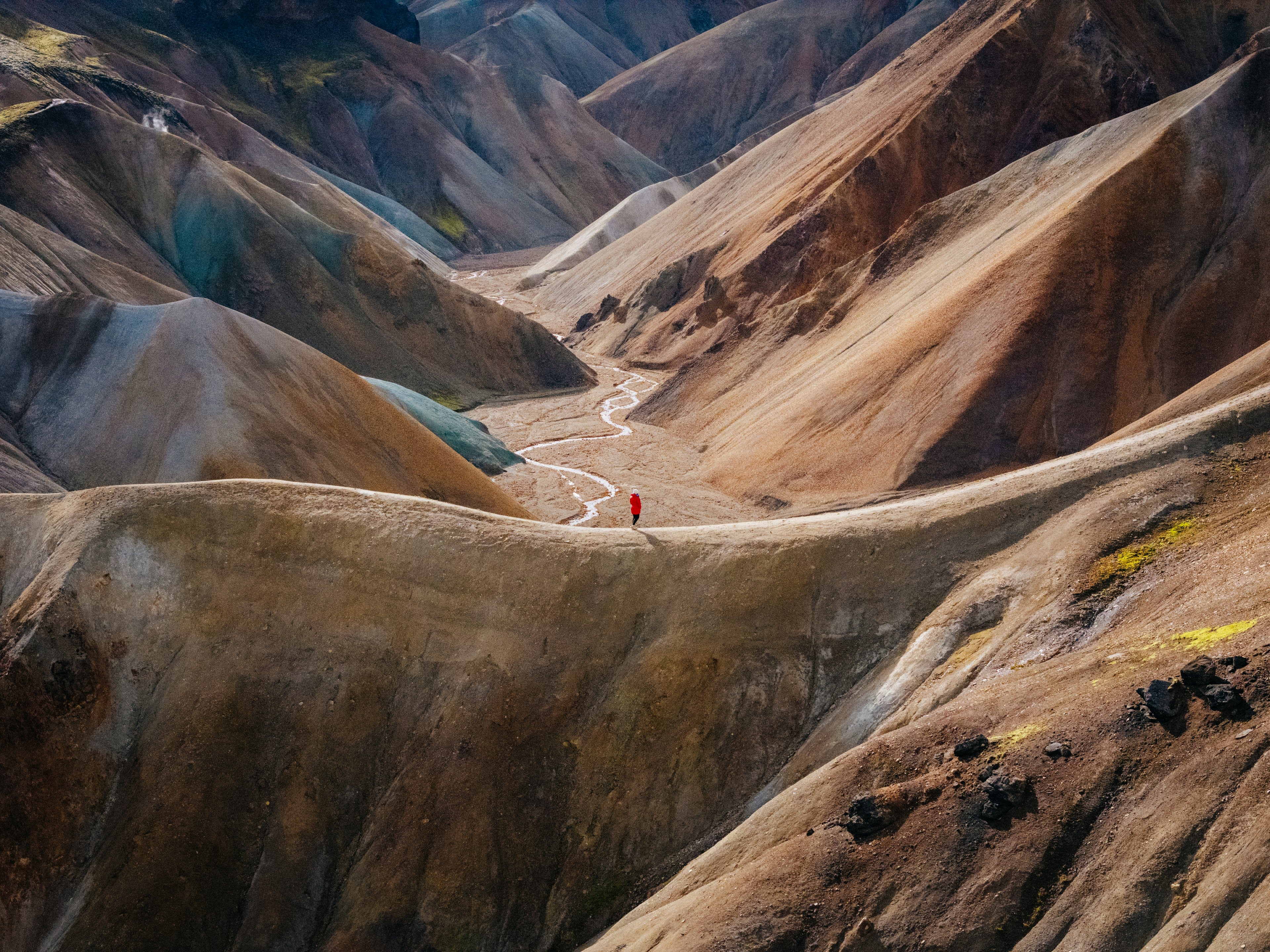 Aerial view of multicoloured rhyolite mountains with a pale track running through the valley