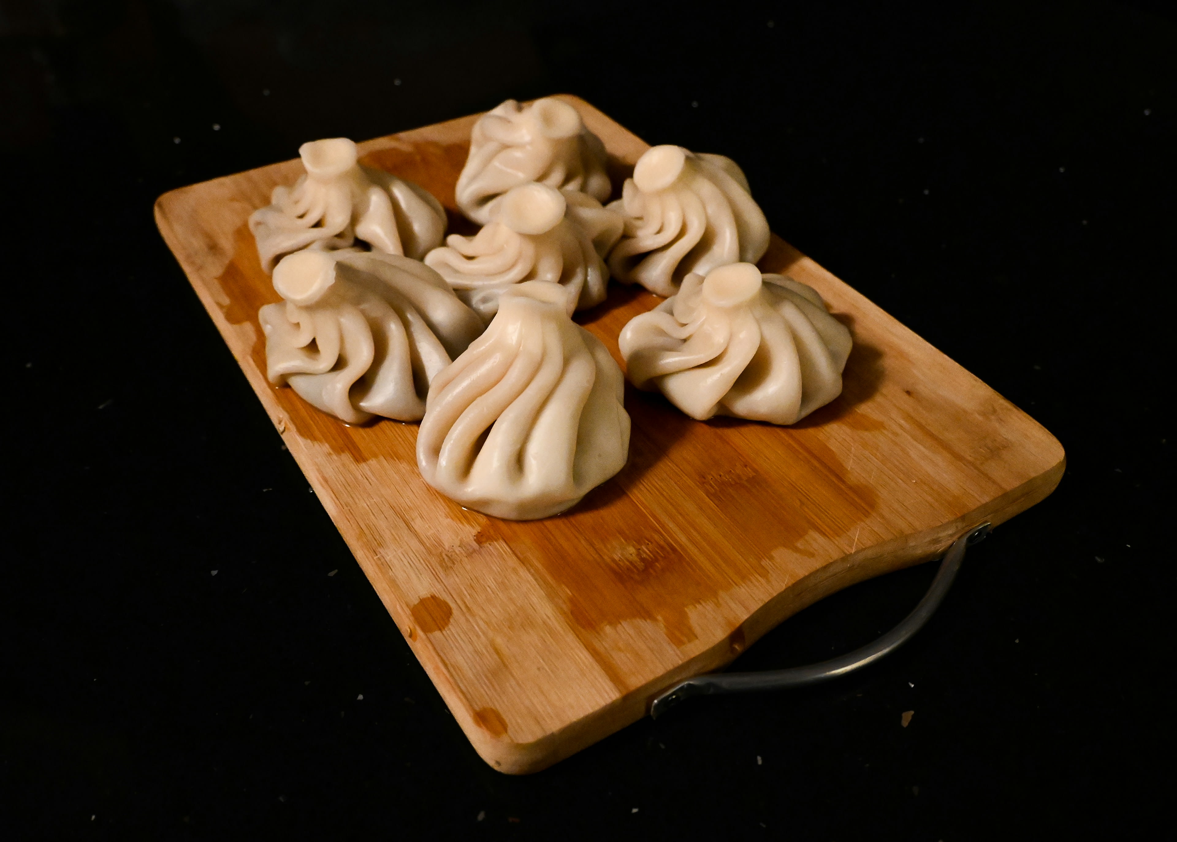 A wooden board of pleated dumplings on a dark table