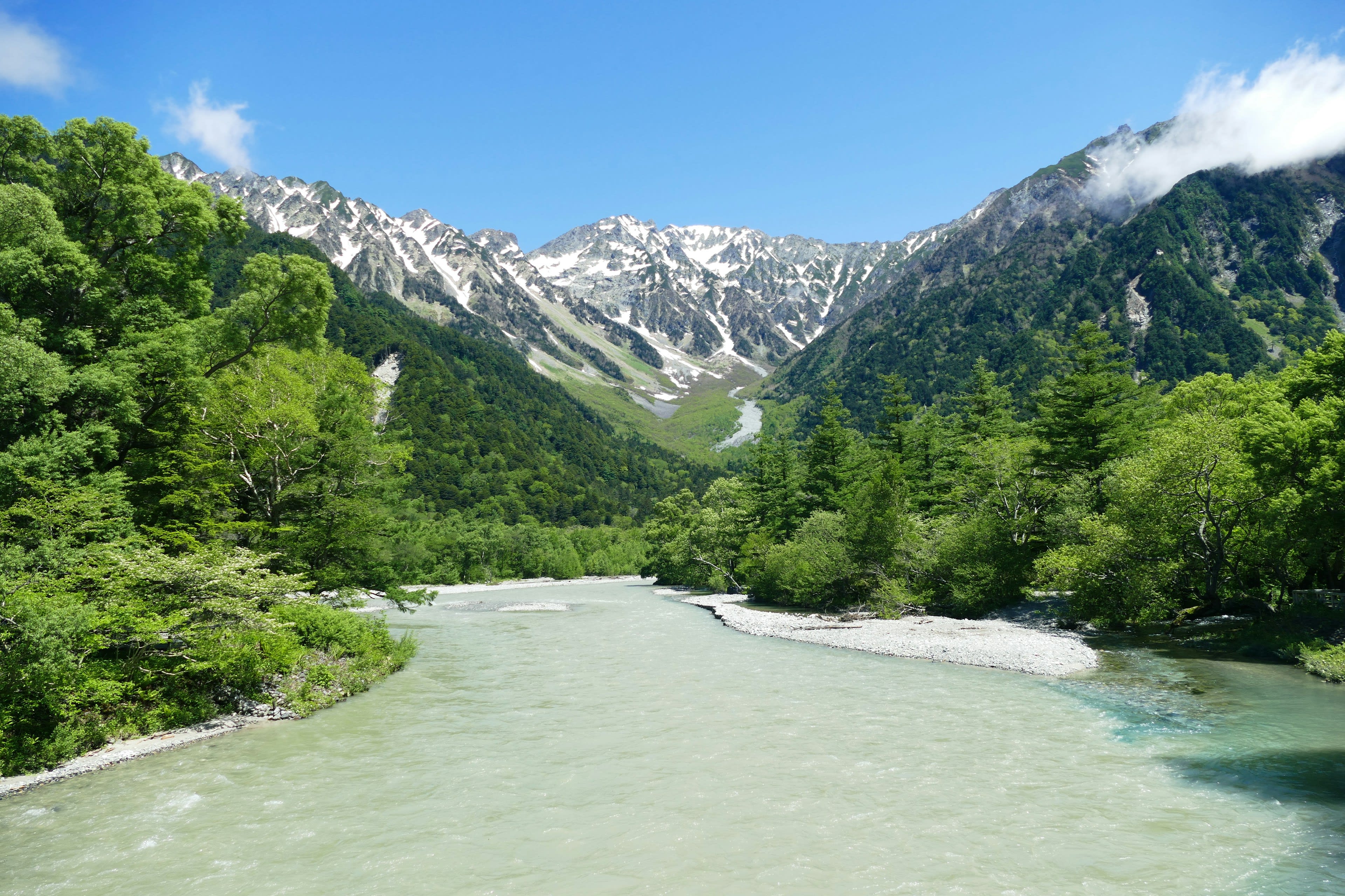 A clear braided river running through a valley below snow-streaked mountains