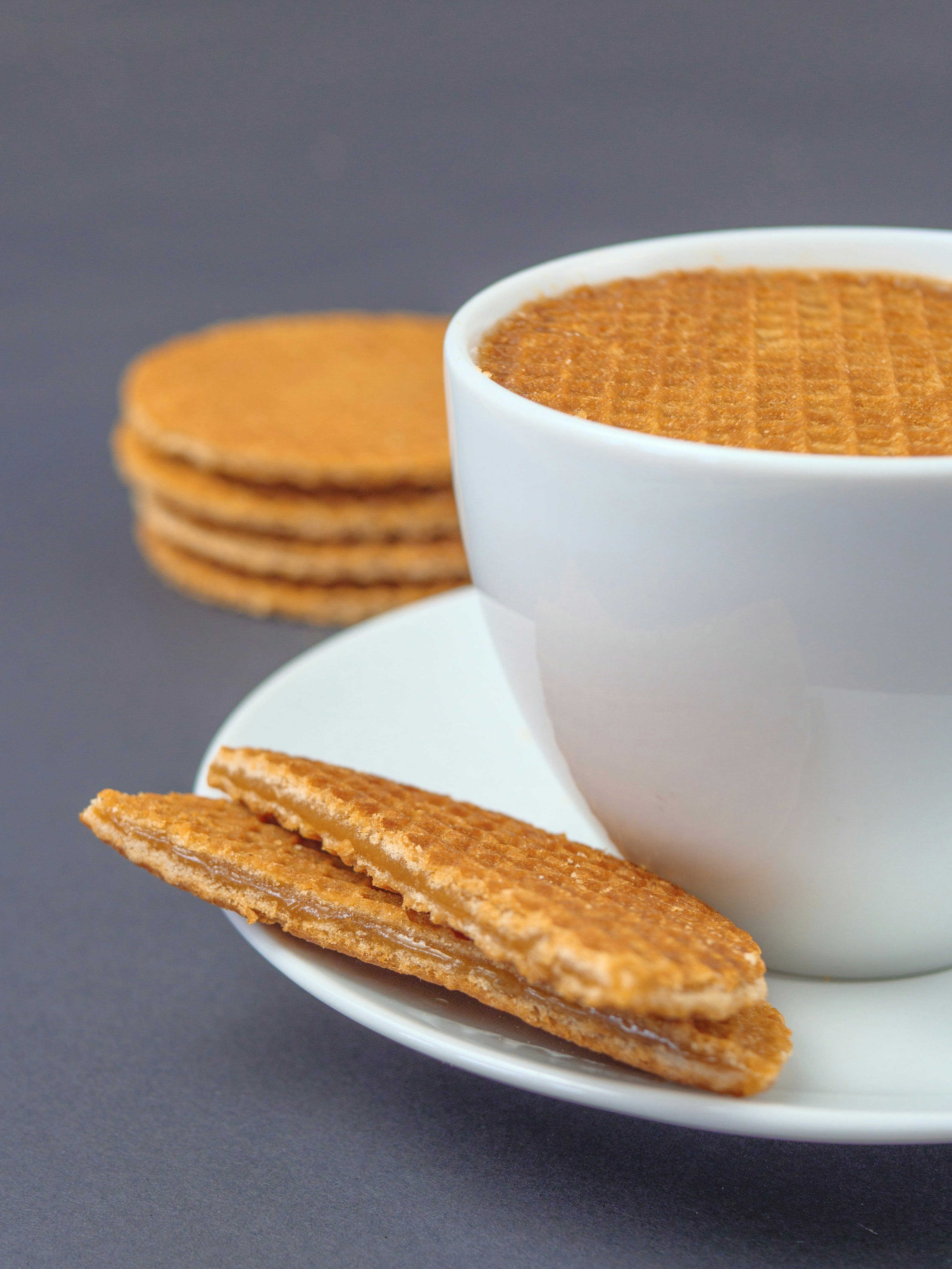 A stroopwafel resting on top of a coffee cup with more stacked beside it