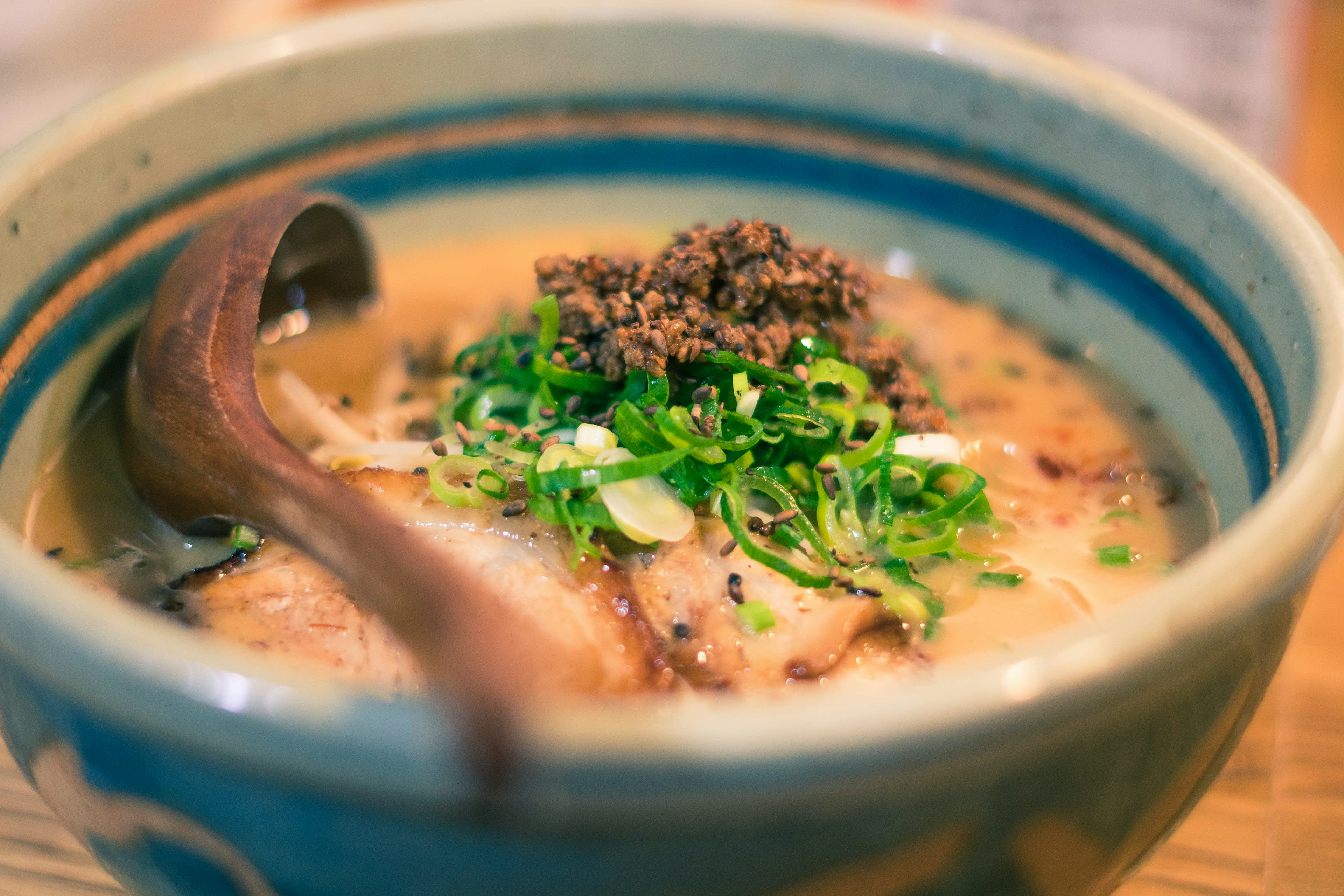 A ceramic bowl of noodles in pale broth with spring onion on a wooden counter
