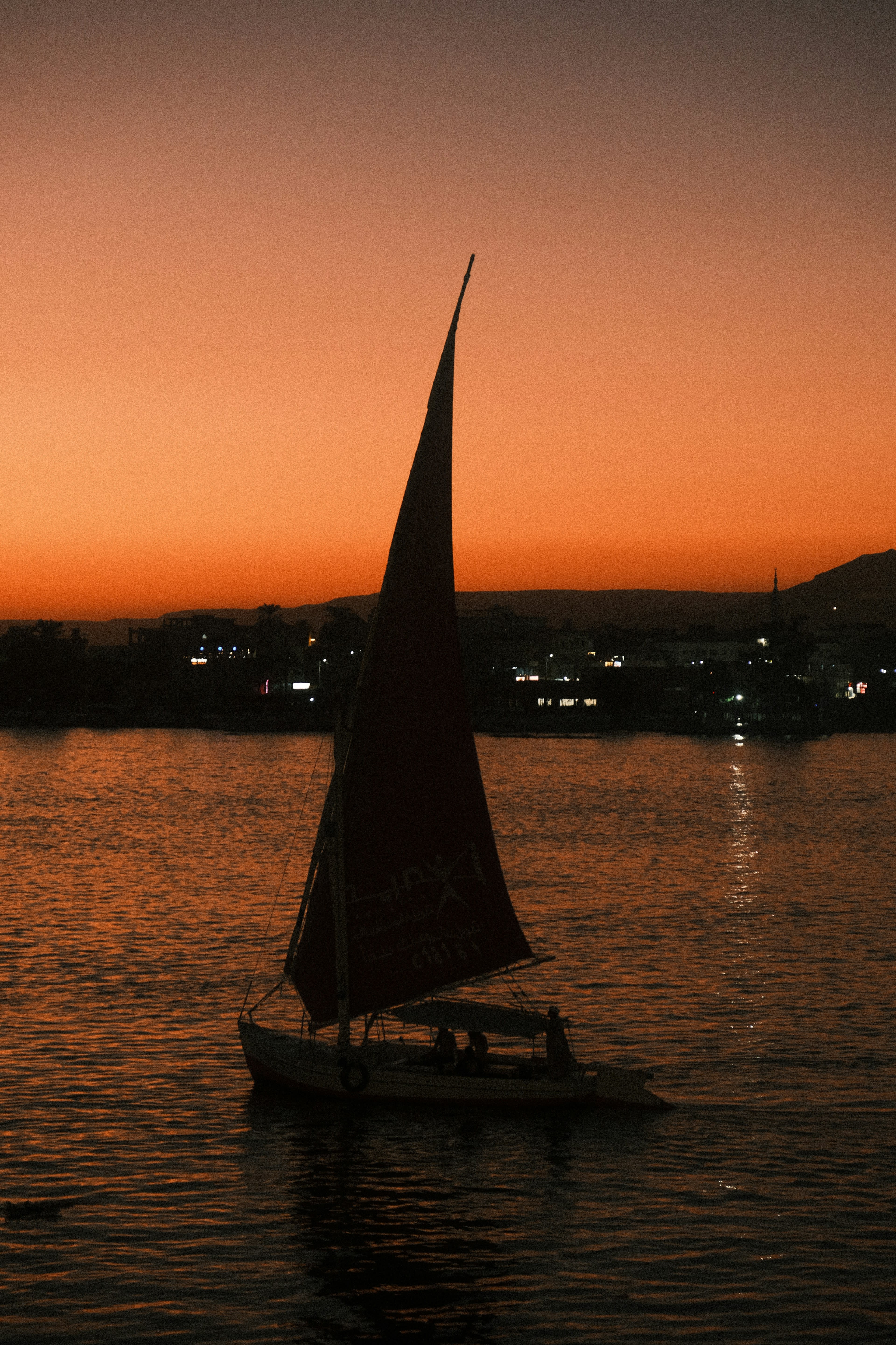 A felucca drifting on the Nile at sunset, its sail catching the last orange light