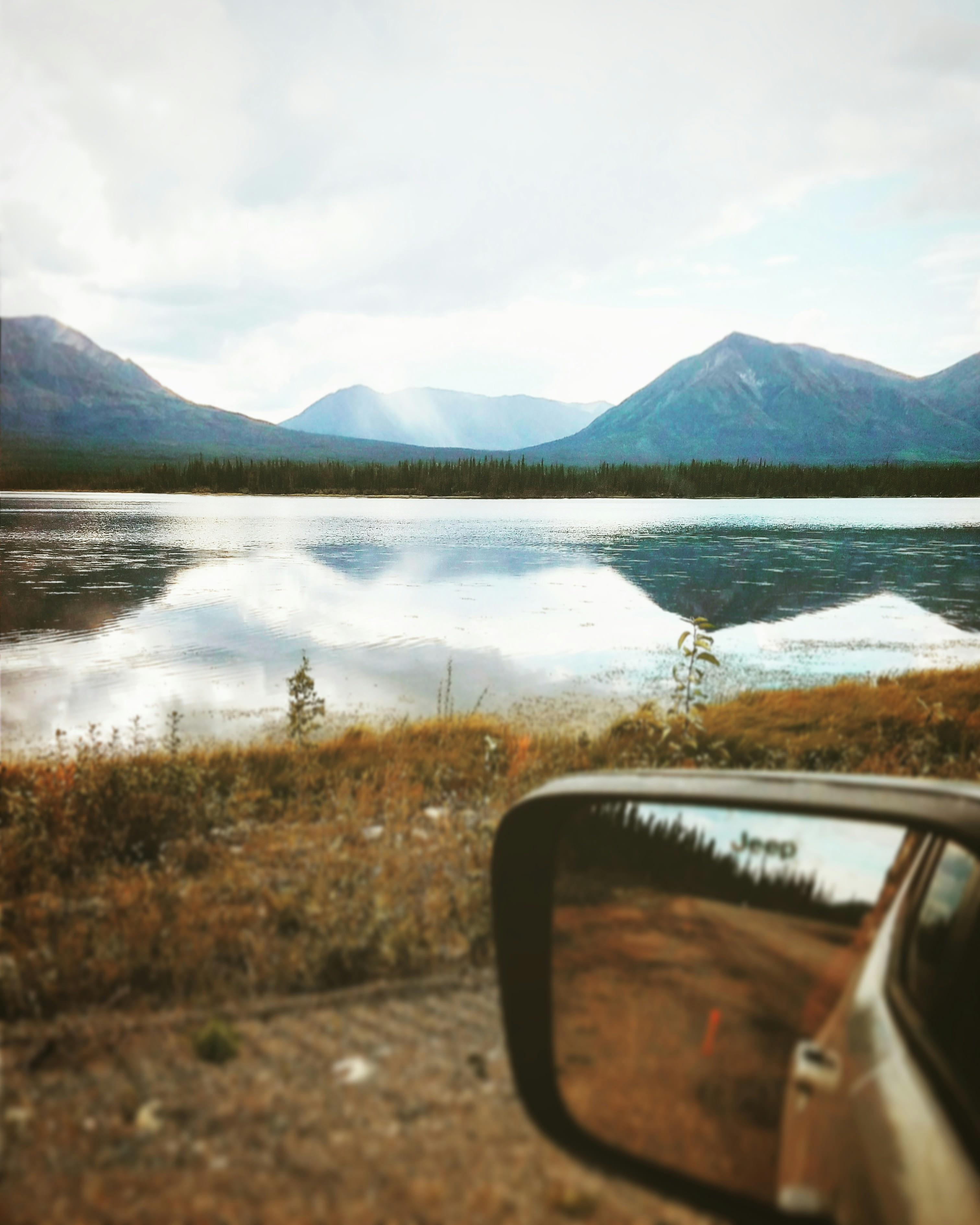 A car wing mirror reflecting a lake and mountains in evening light