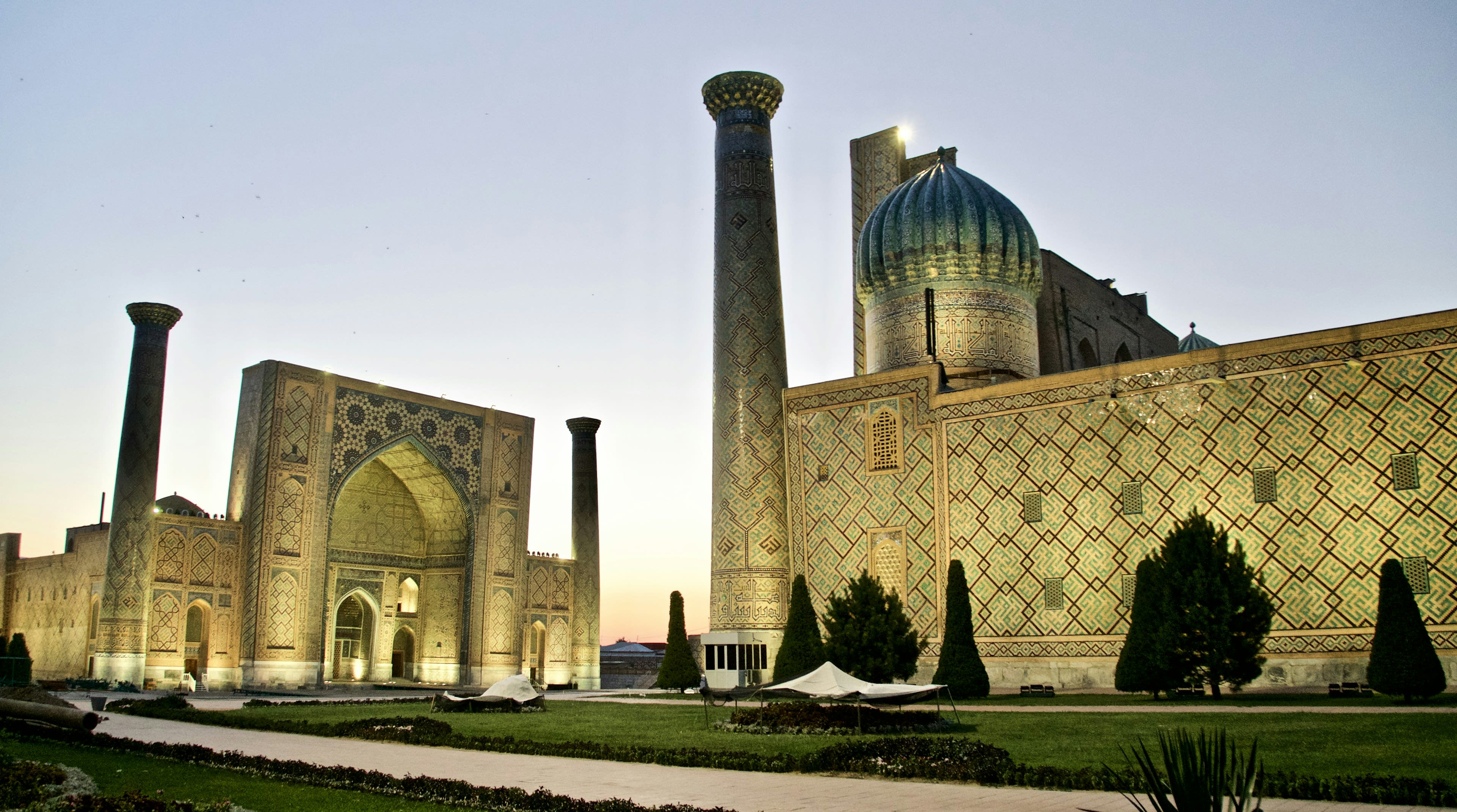 Three tiled madrasas facing a wide square in evening light
