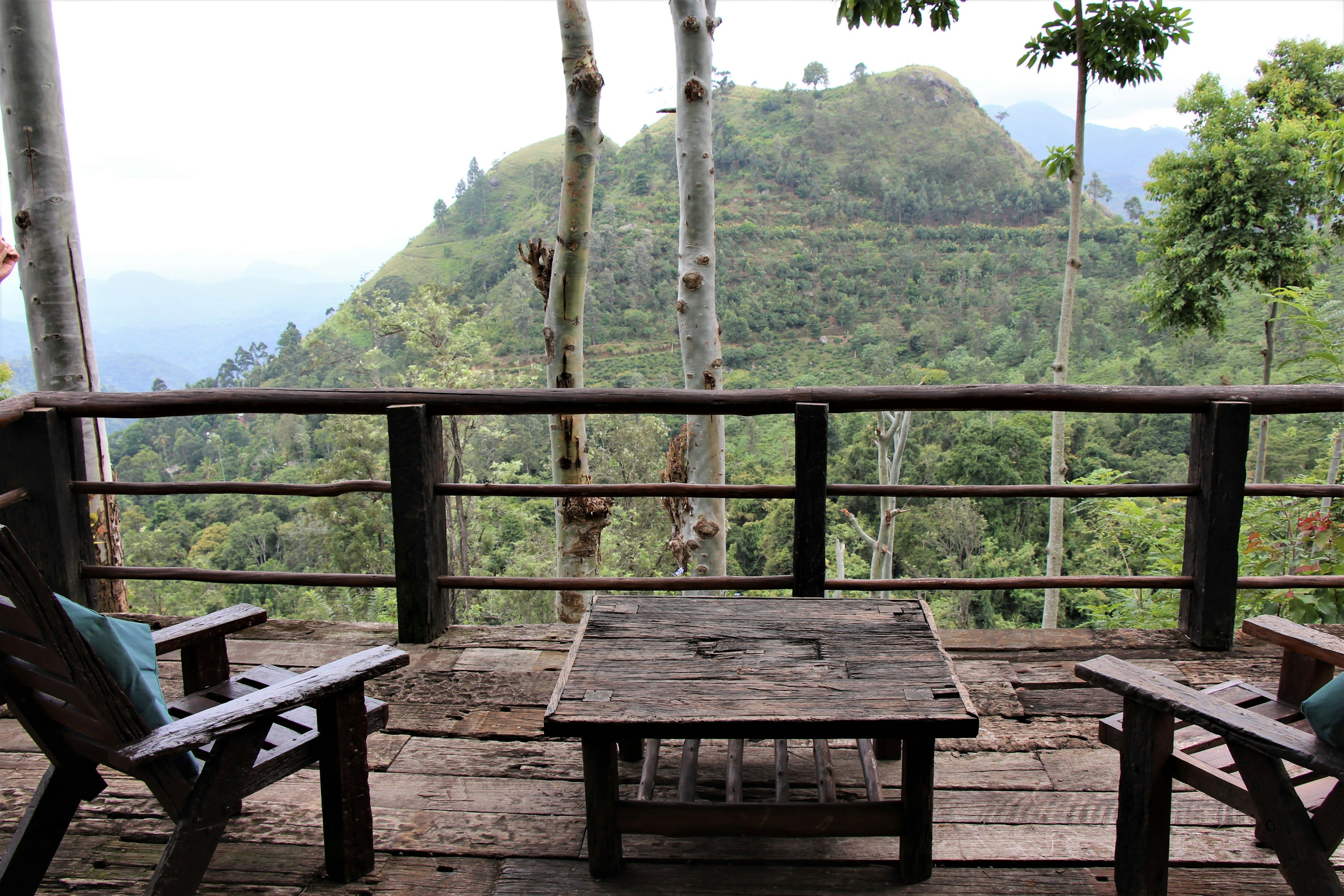 Wooden chairs and a table on a balcony overlooking a misty green valley