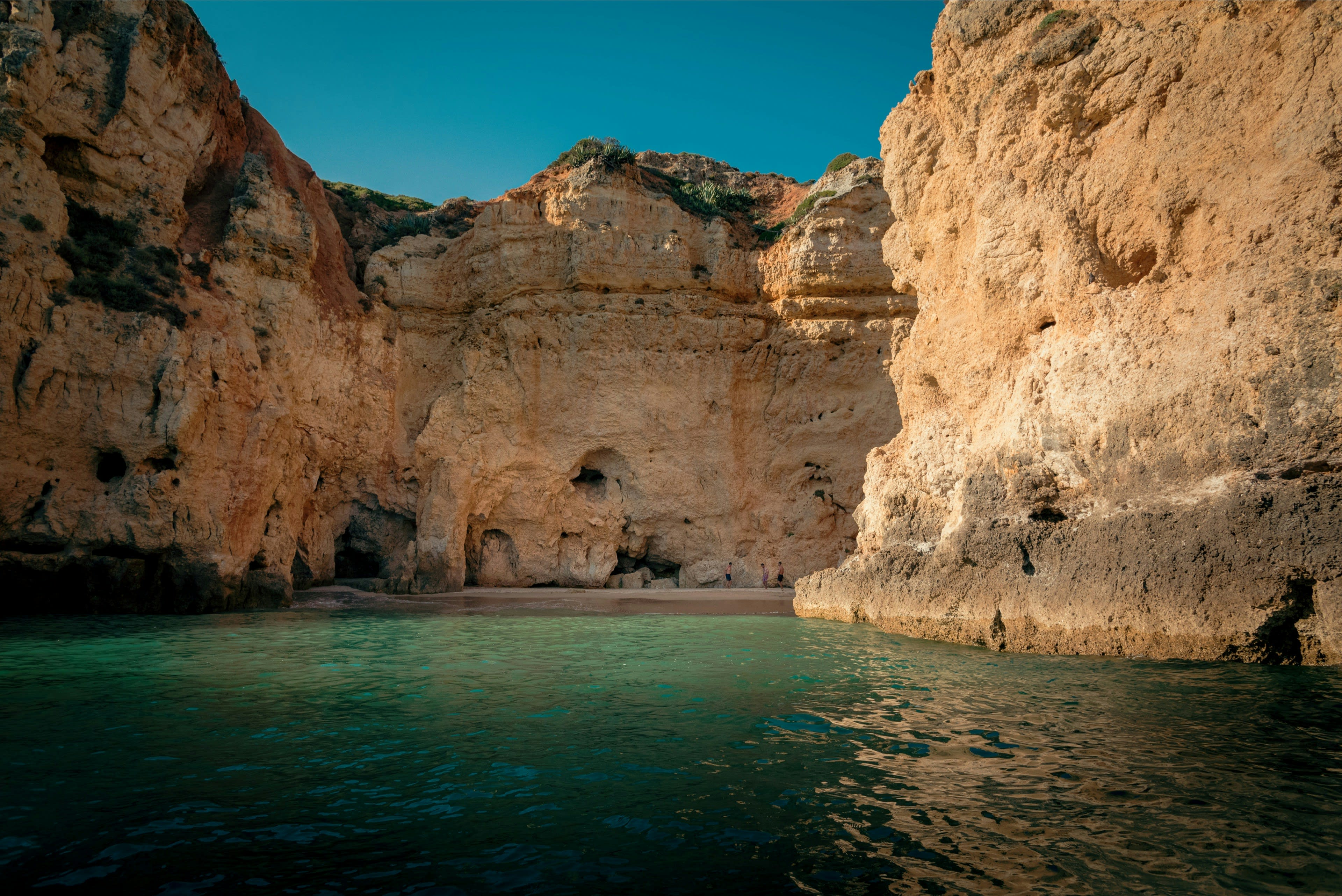 Golden rock walls of a sea cave seen from a boat on green water