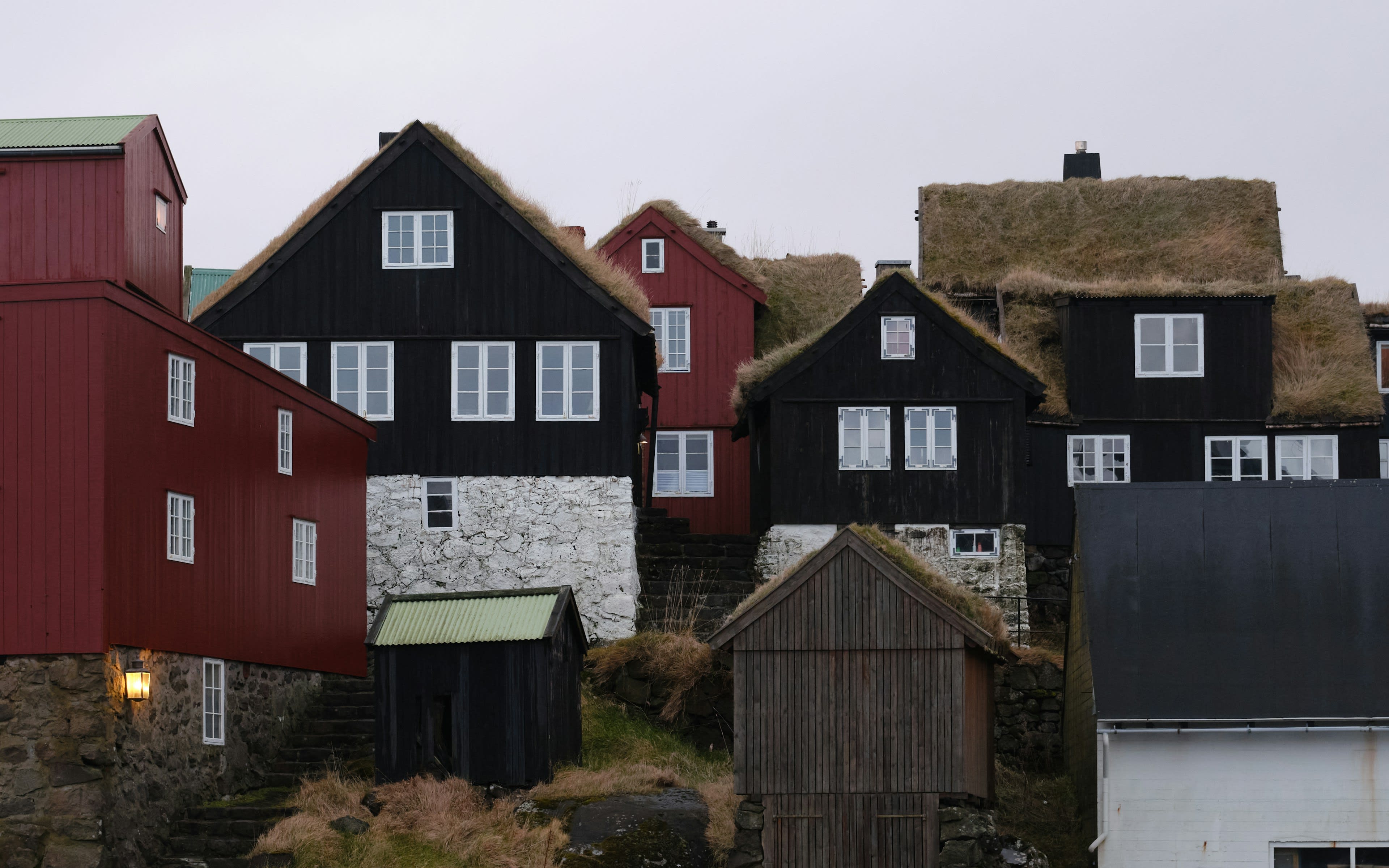 Red-painted timber houses with turf roofs on a rocky harbour spit at dusk