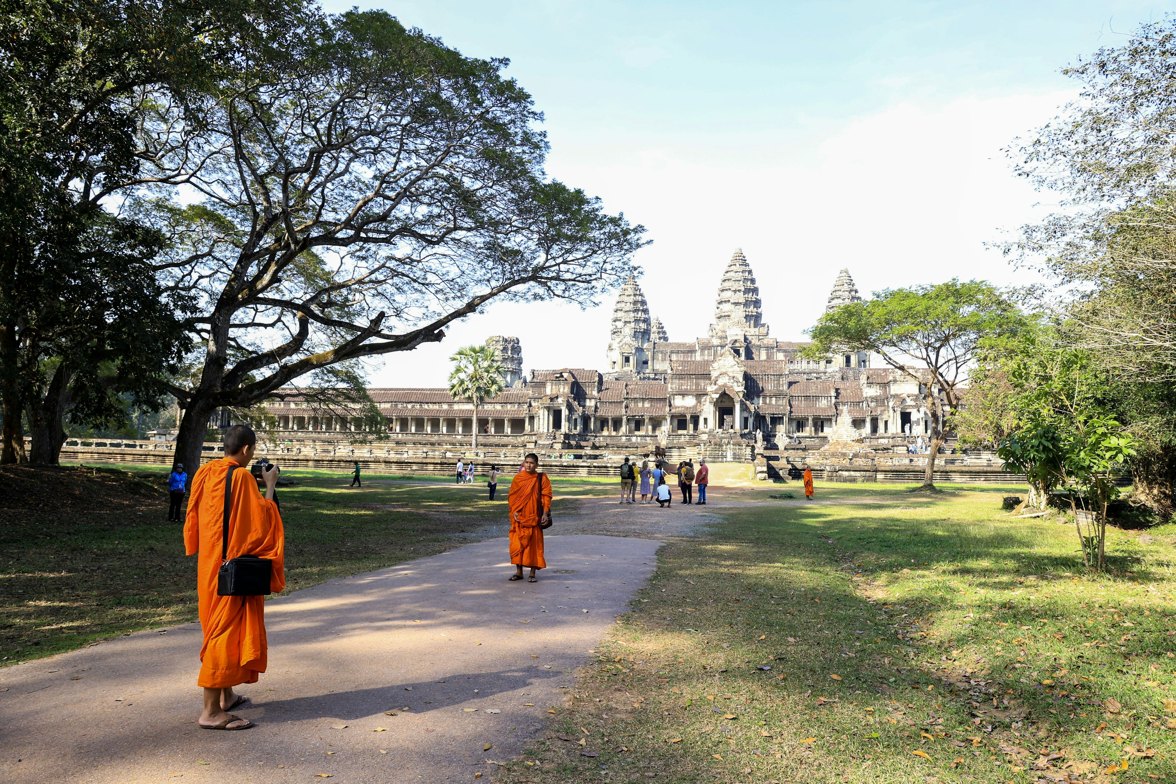 Monks in orange robes walking before a grey stone temple