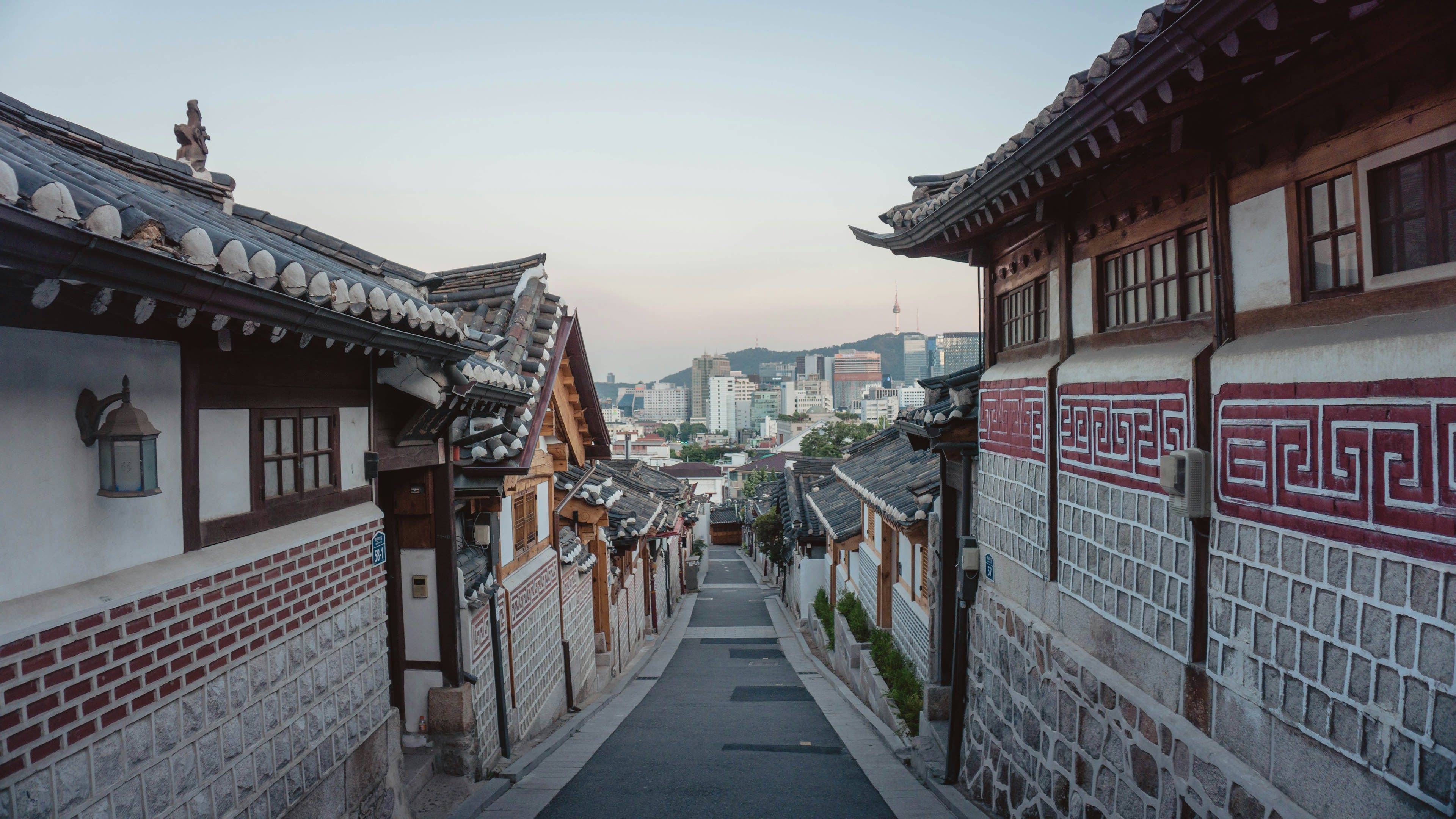 A steep alley of traditional tiled Korean houses with a tower on the skyline beyond