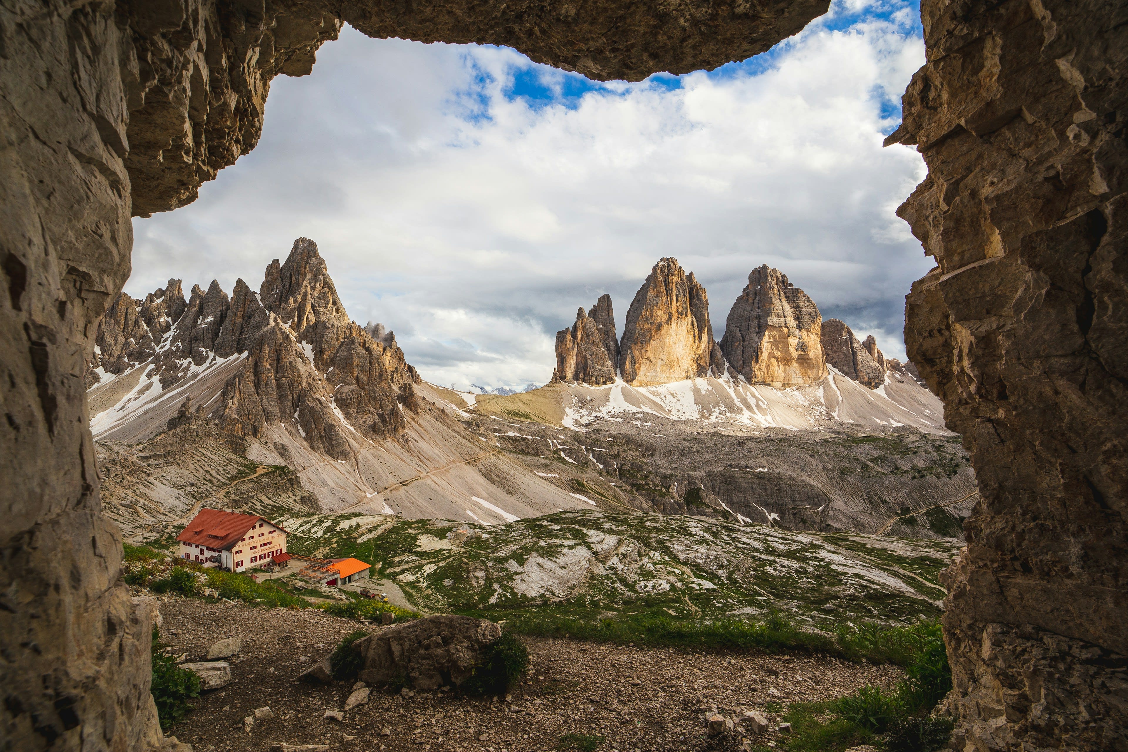 Jagged Dolomite spires framed by the mouth of a rock cave, with red tents far below