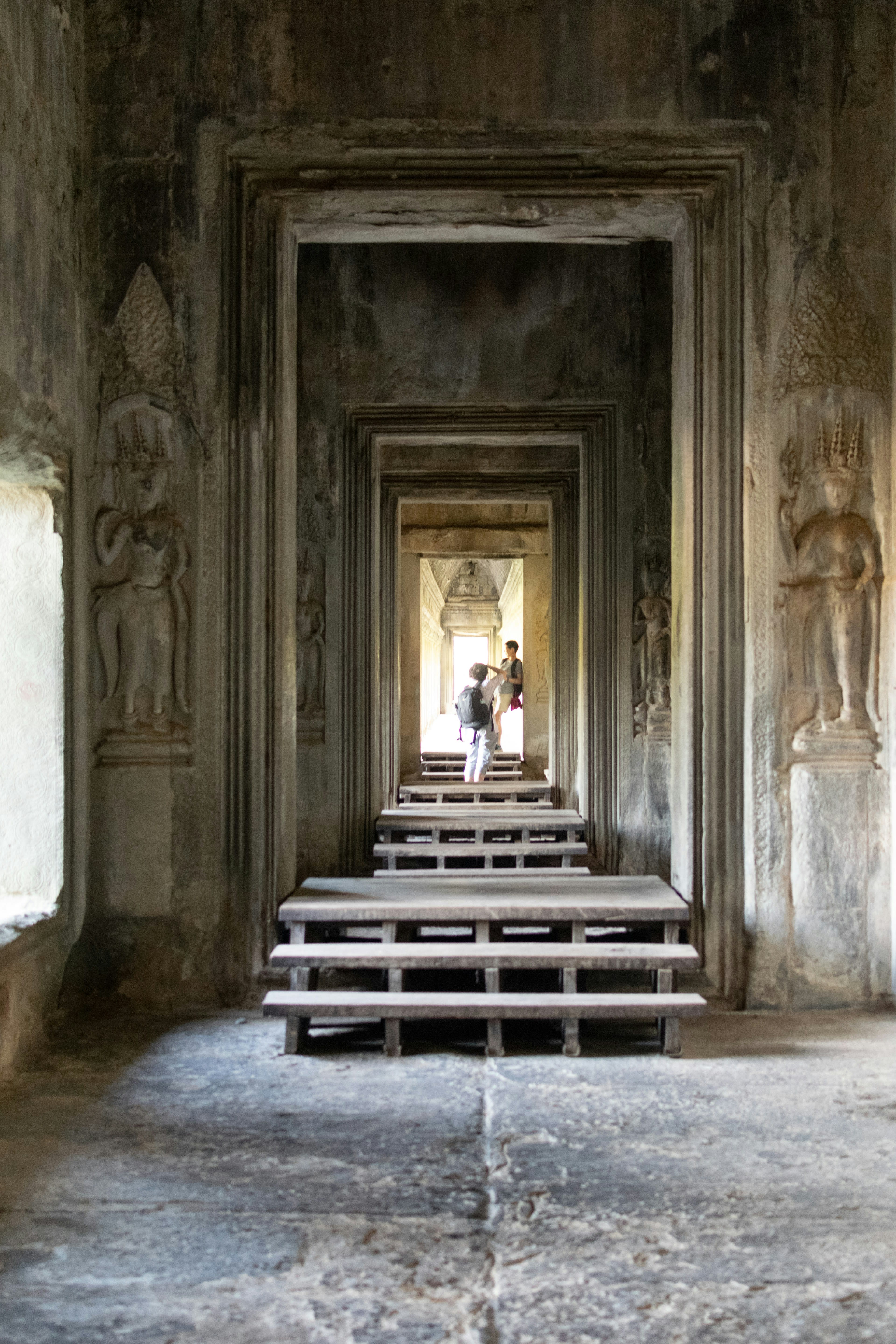 A long stone temple corridor with a figure seated far down it
