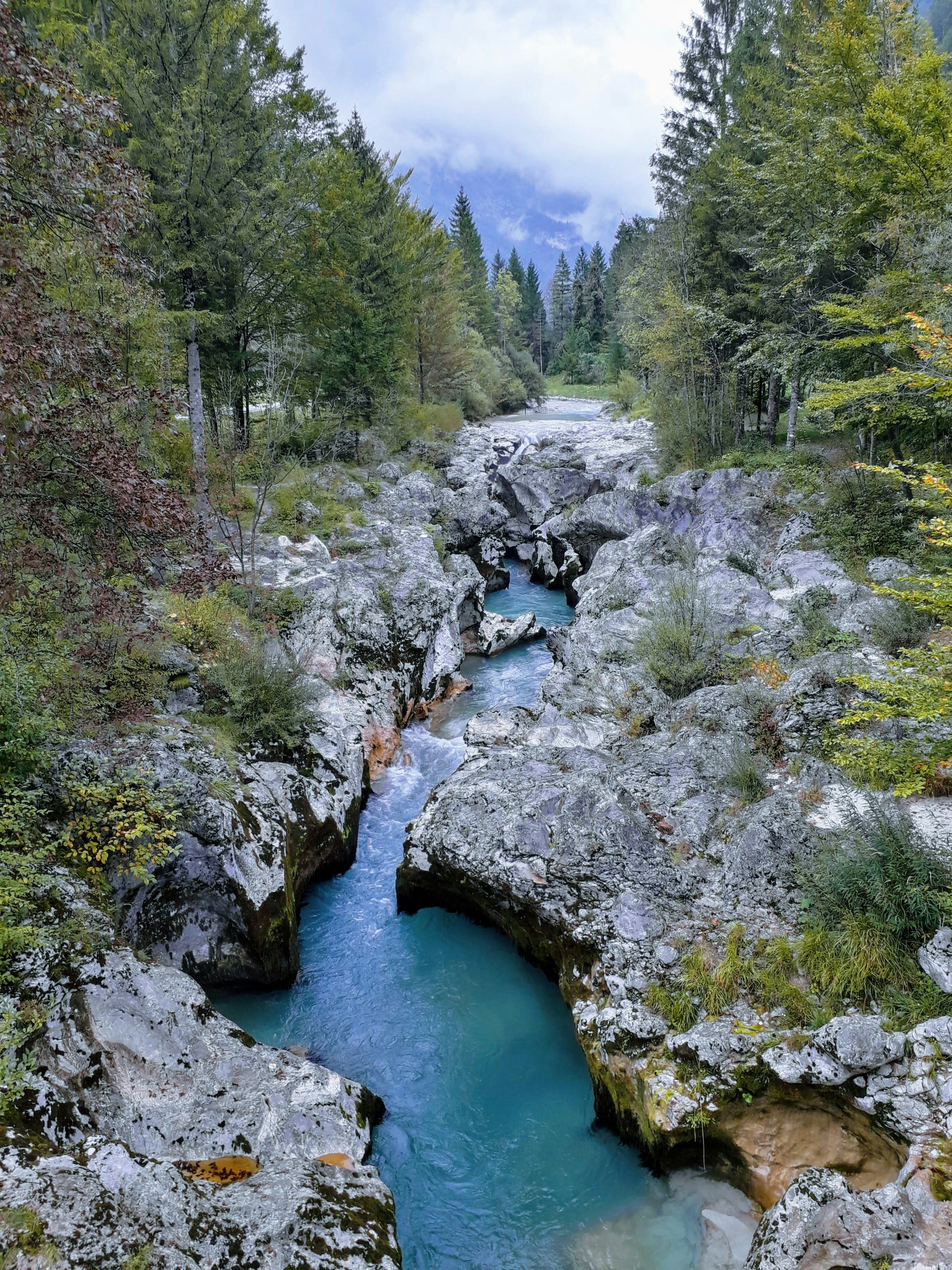 A narrow turquoise river running between white stone walls and green trees