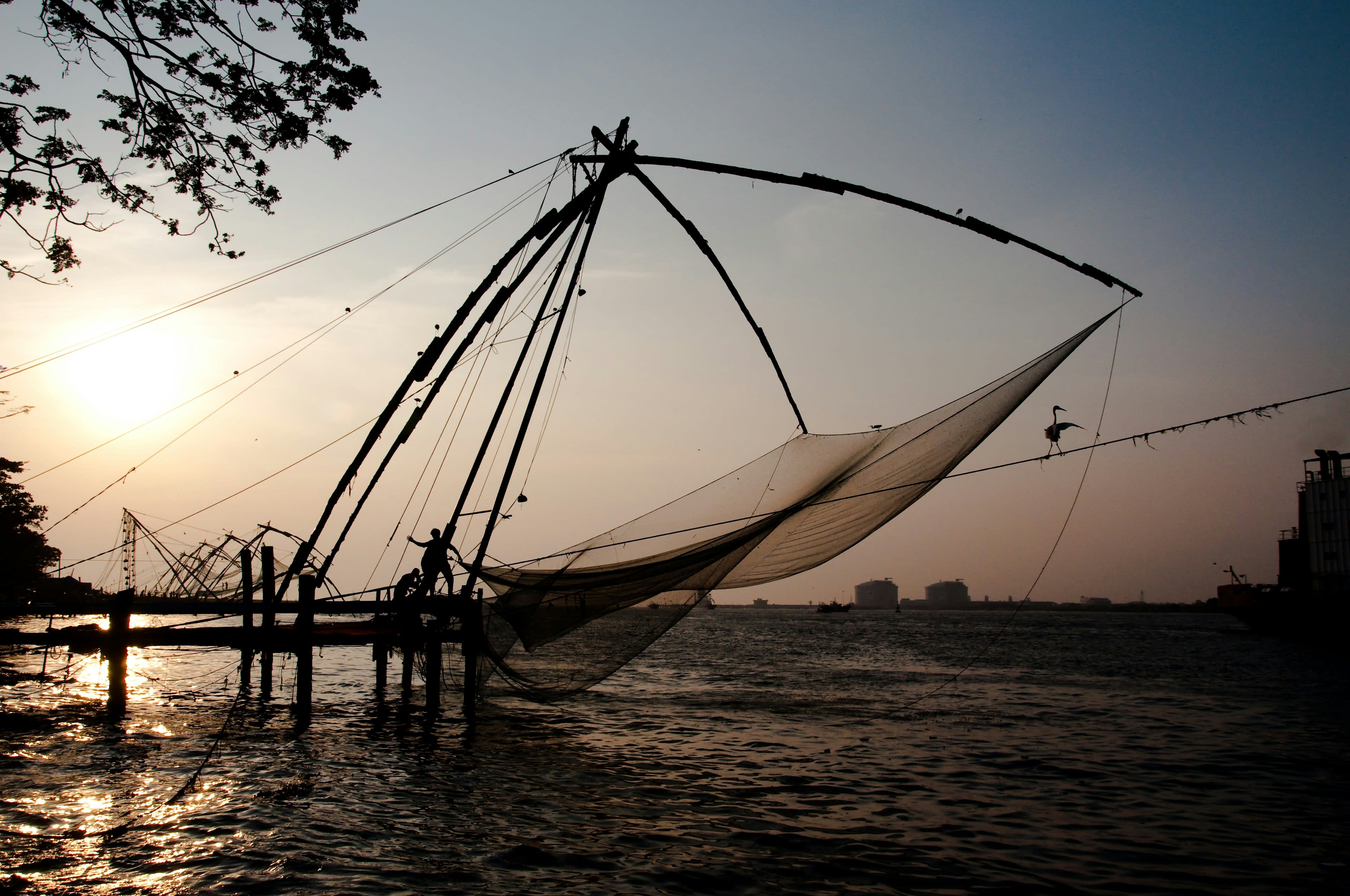 Cantilevered Chinese fishing nets silhouetted against a low sun over the harbour