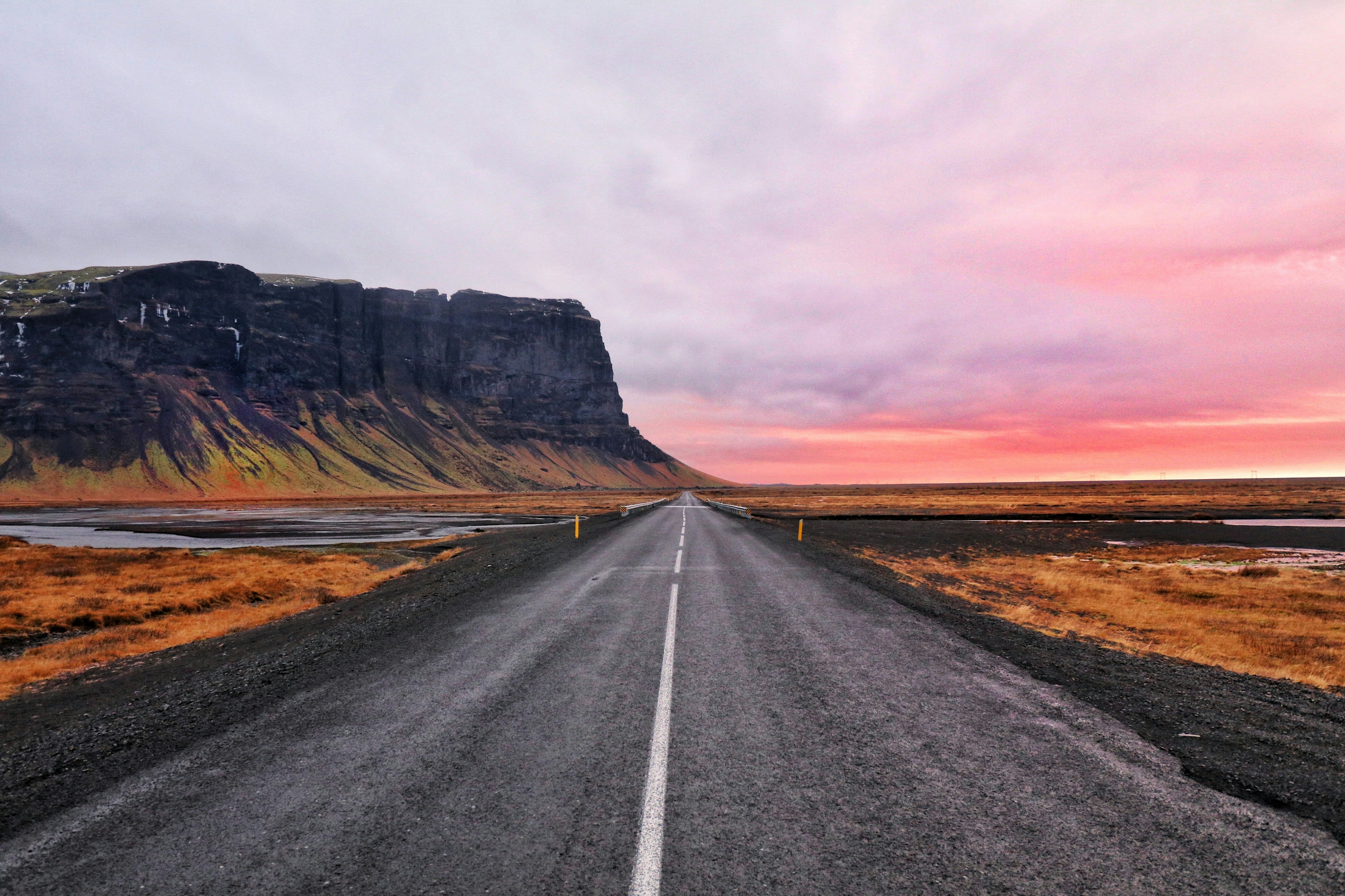 An empty asphalt road running towards a dark flat-topped mountain under a pink dawn sky