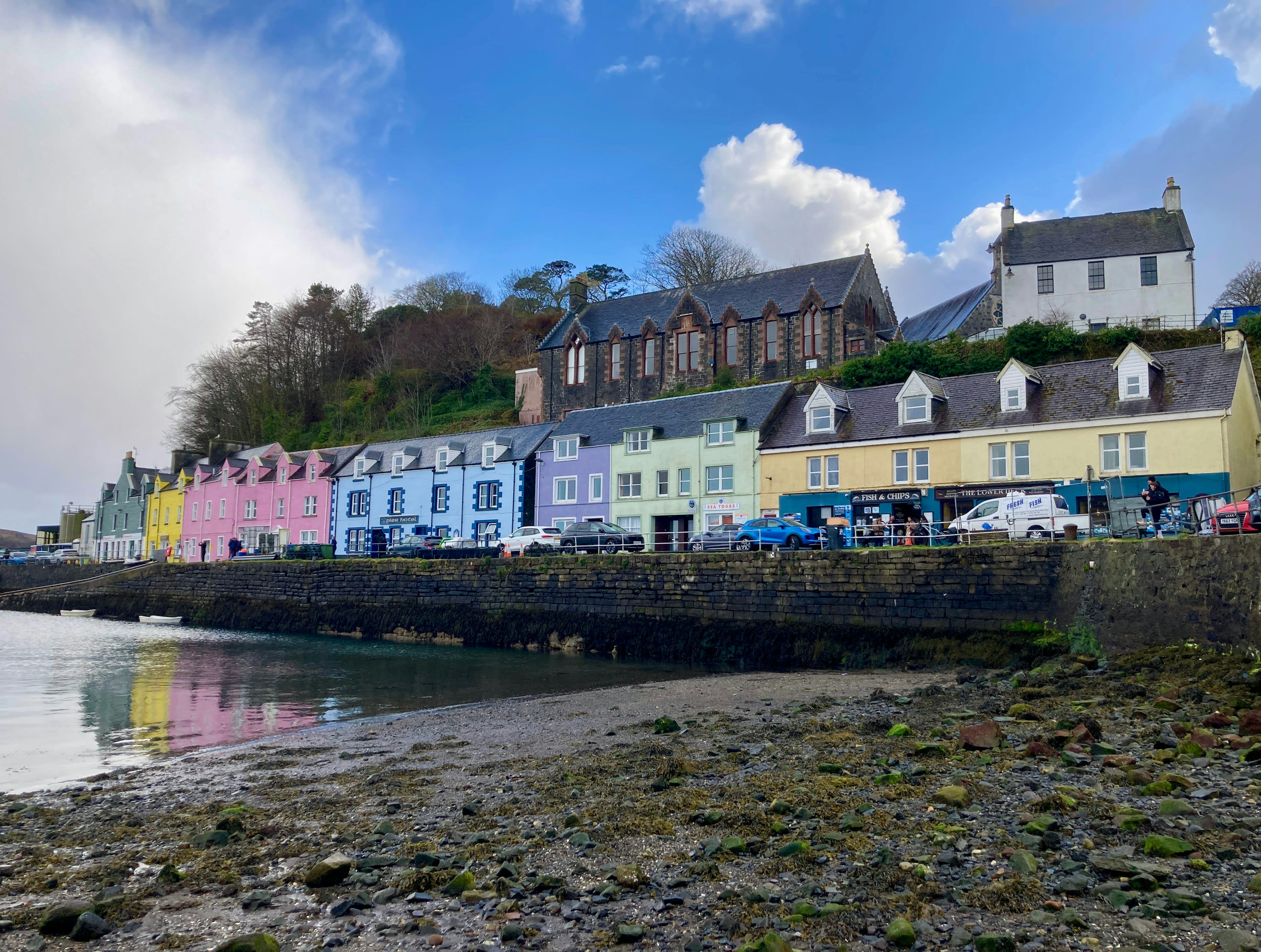 A row of pastel-painted houses along a harbour front above a shingle beach
