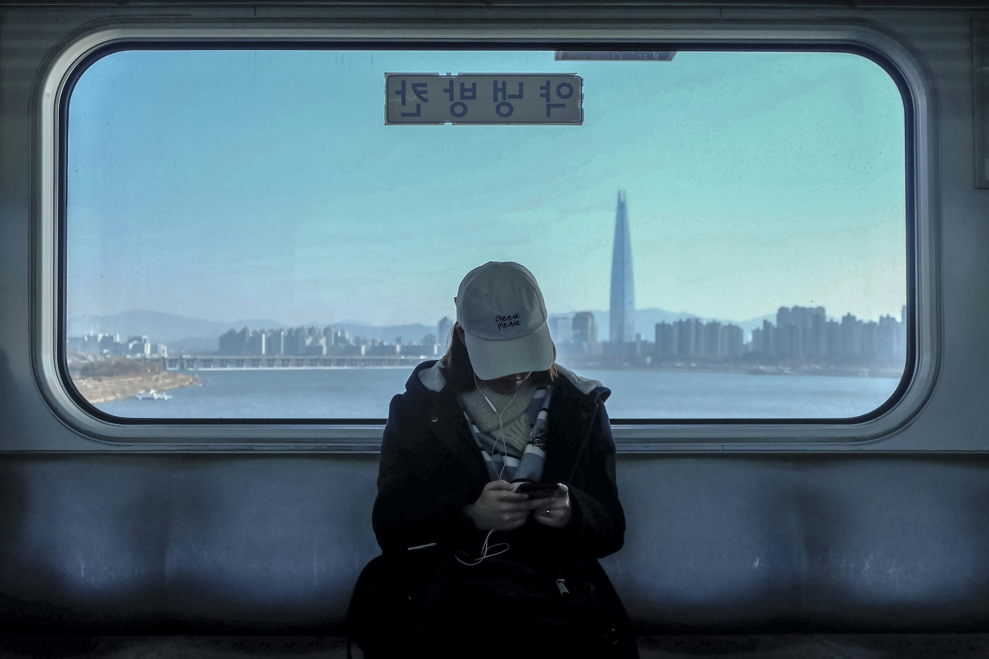 A seated passenger silhouetted against a train window showing a river and a tall tower beyond